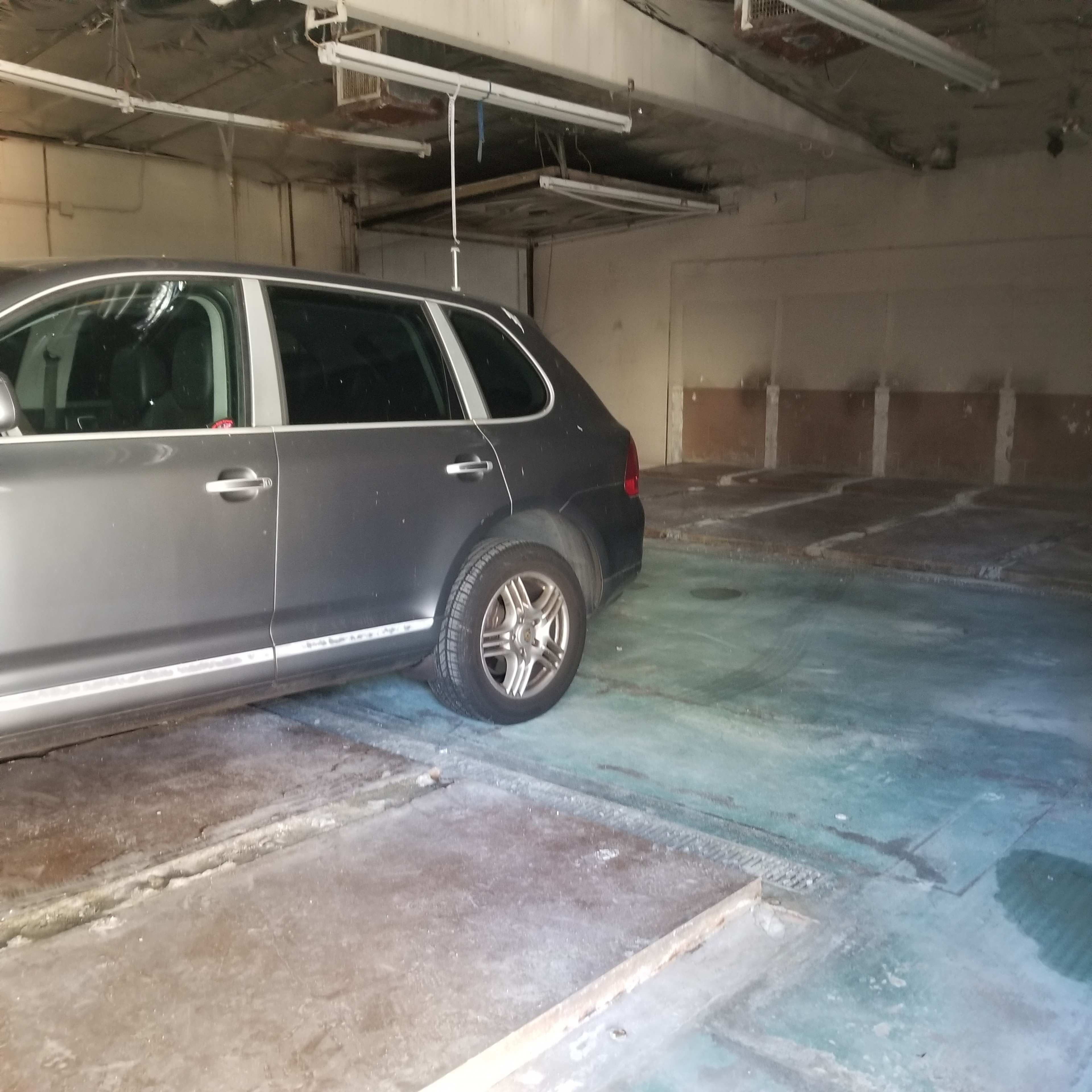 A dark-colored SUV is parked in an empty, partially cluttered garage with concrete flooring.