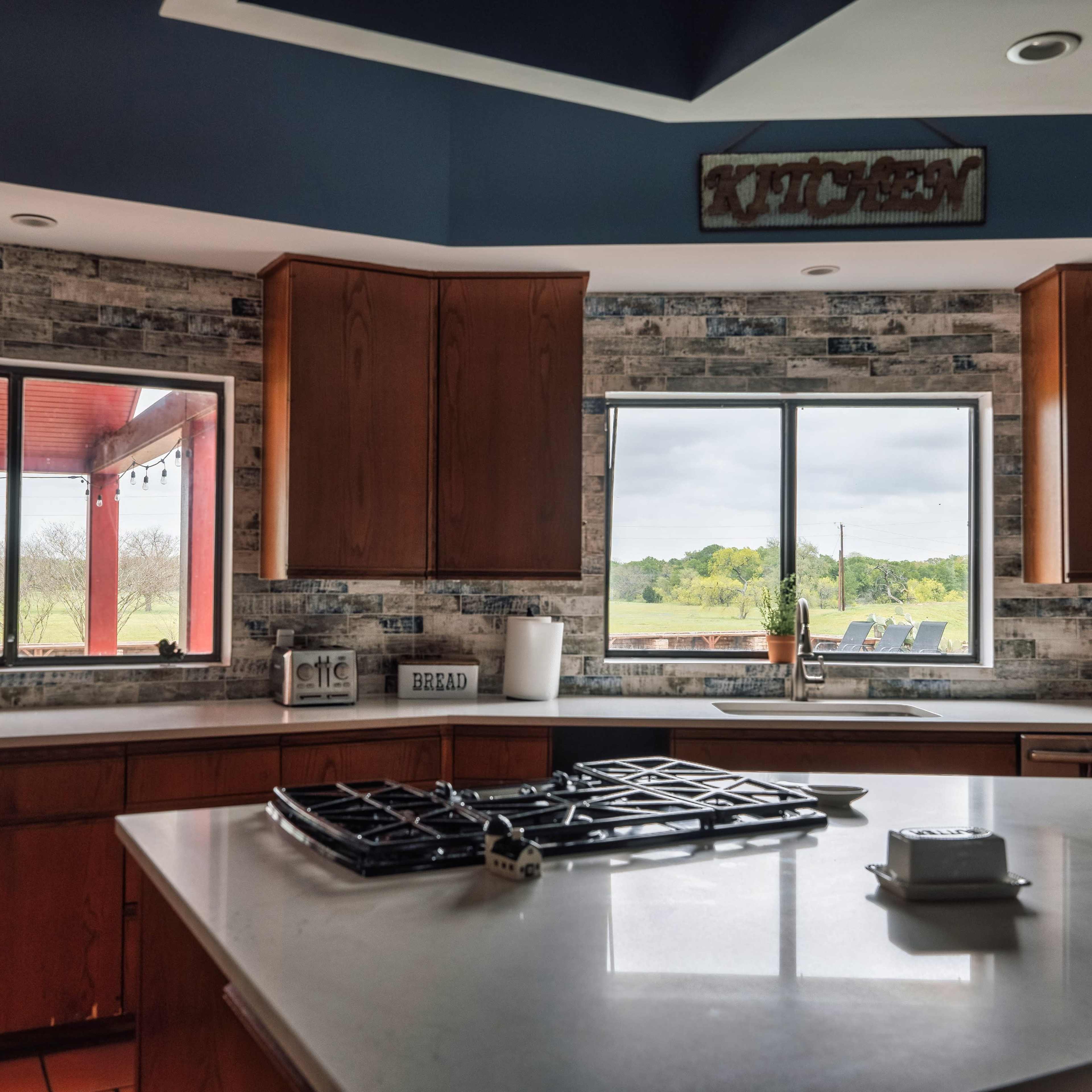 A modern kitchen with wooden cabinets and large windows overlooking a green landscape.