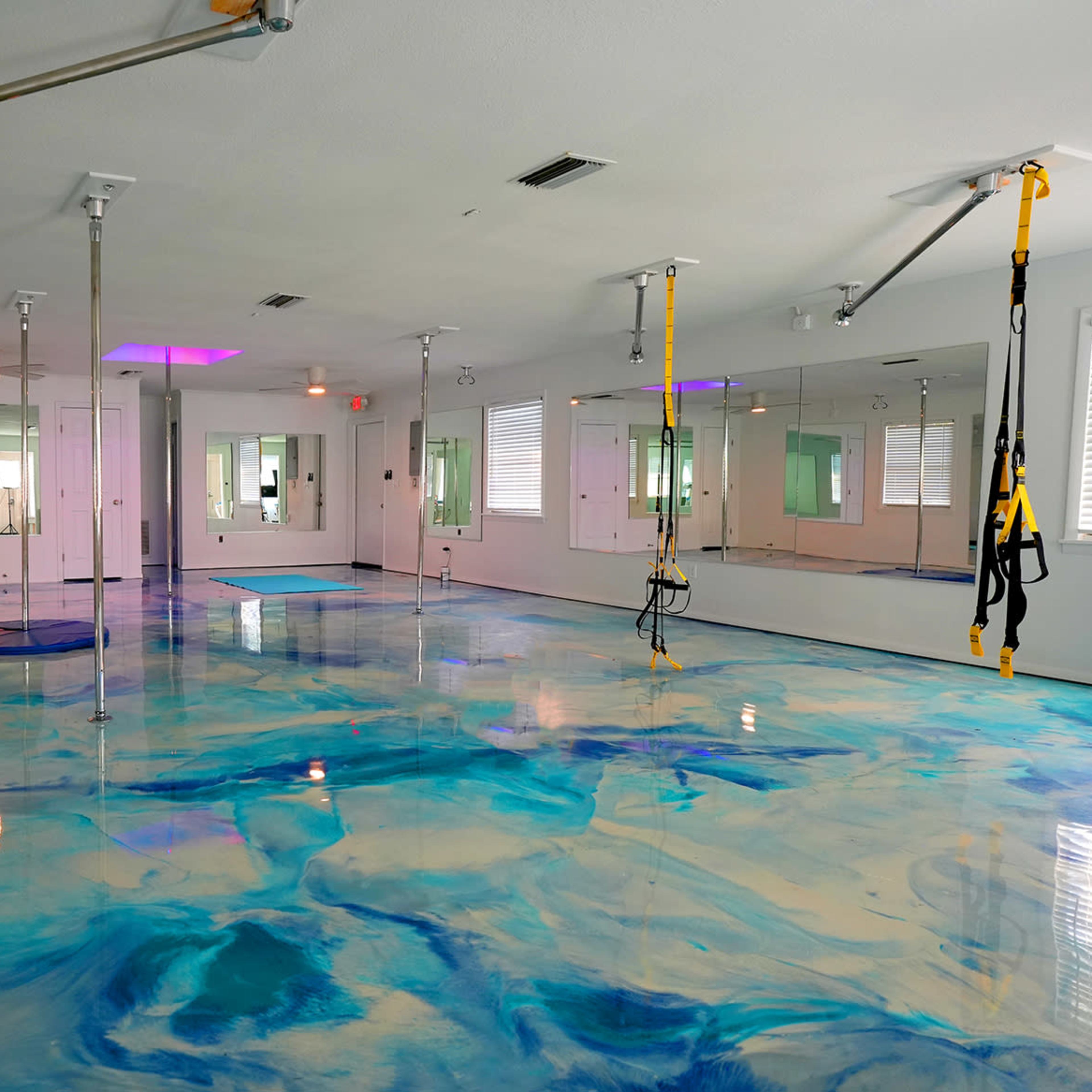 A spacious room with a glossy, blue-and-white marbled floor, equipped with mirrors and suspension training equipment hanging from the ceiling.