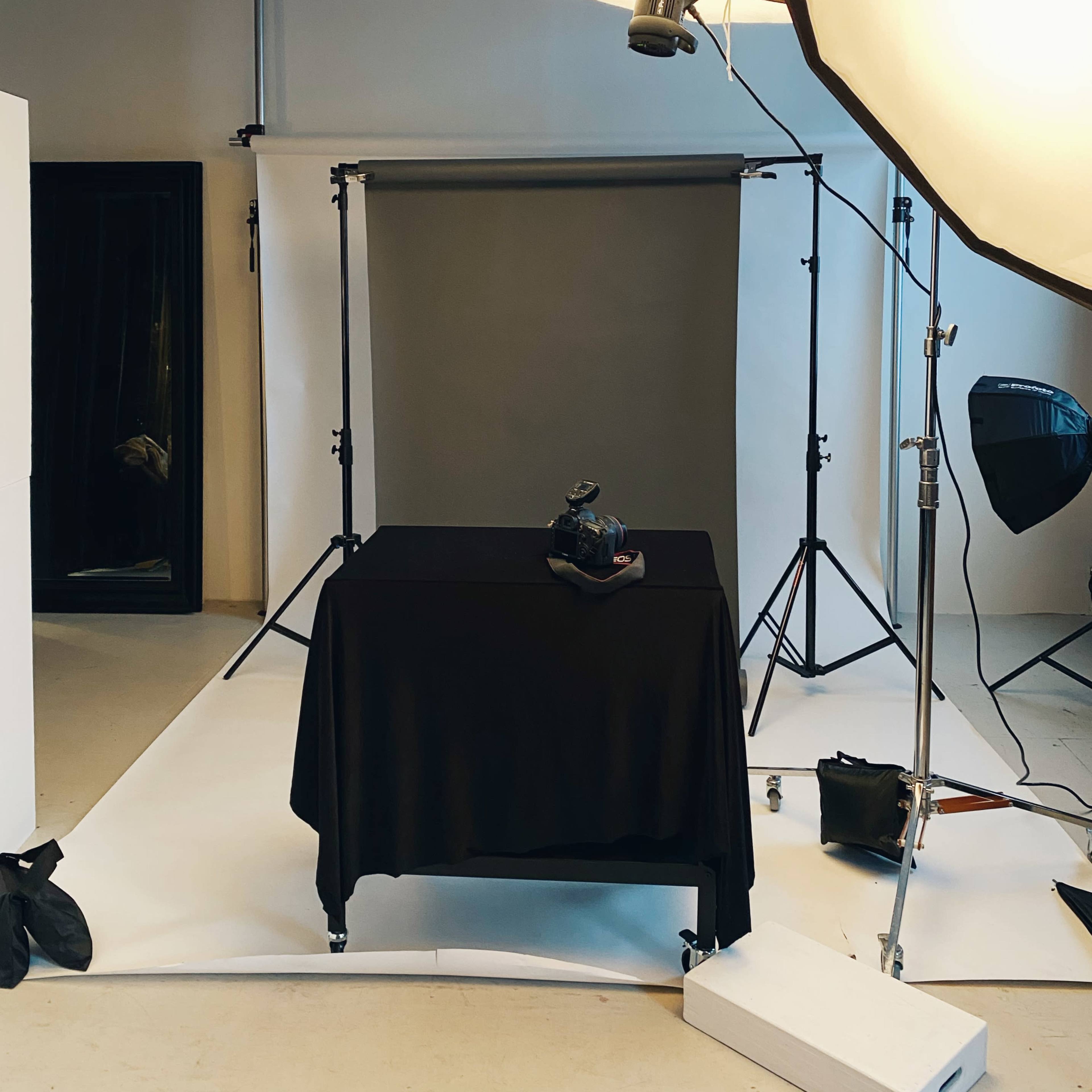 A photography studio setup with a black table, a backdrop, and large lighting equipment.