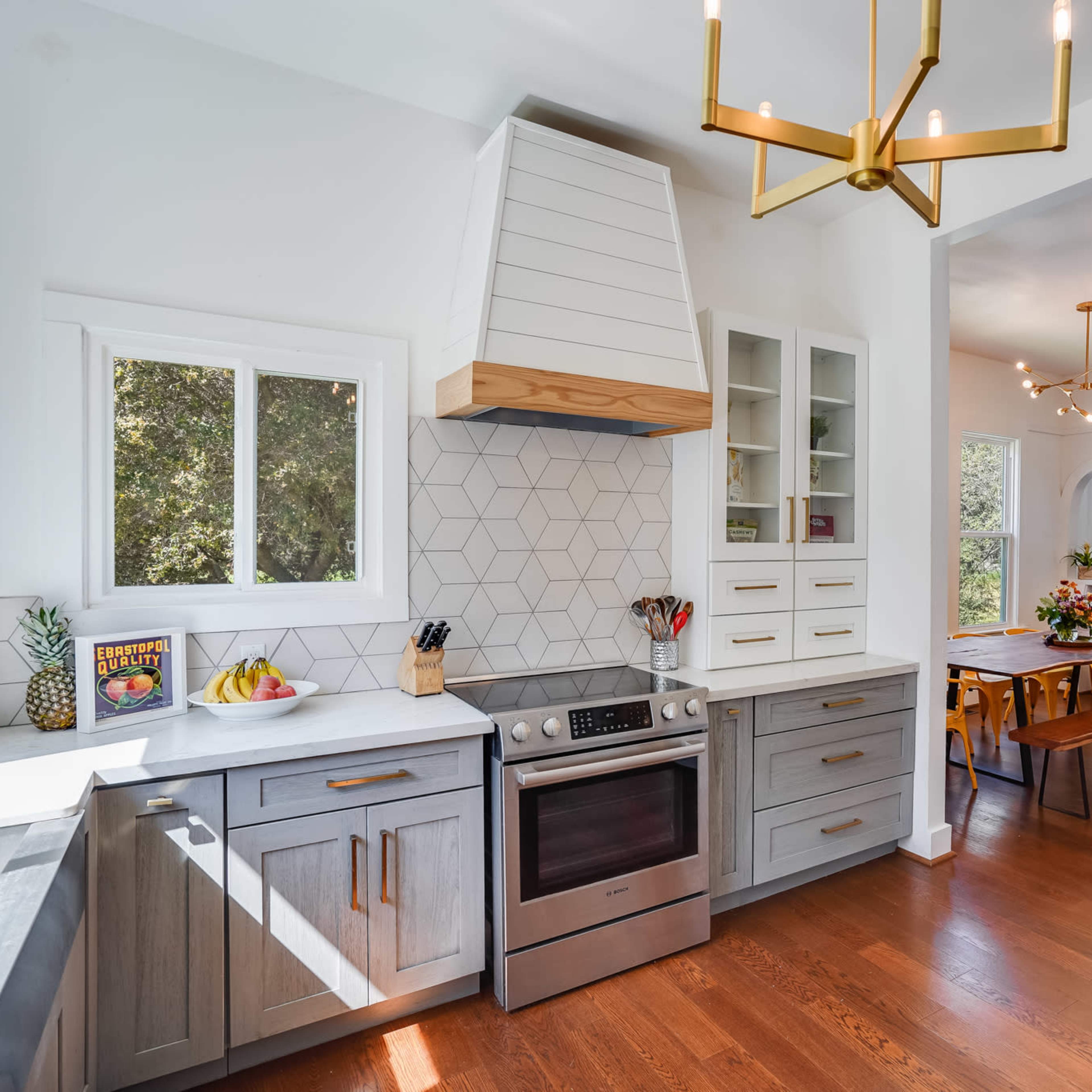 A modern kitchen features a stainless steel oven, a geometric tile backsplash, and a large island with natural light streaming through the windows.