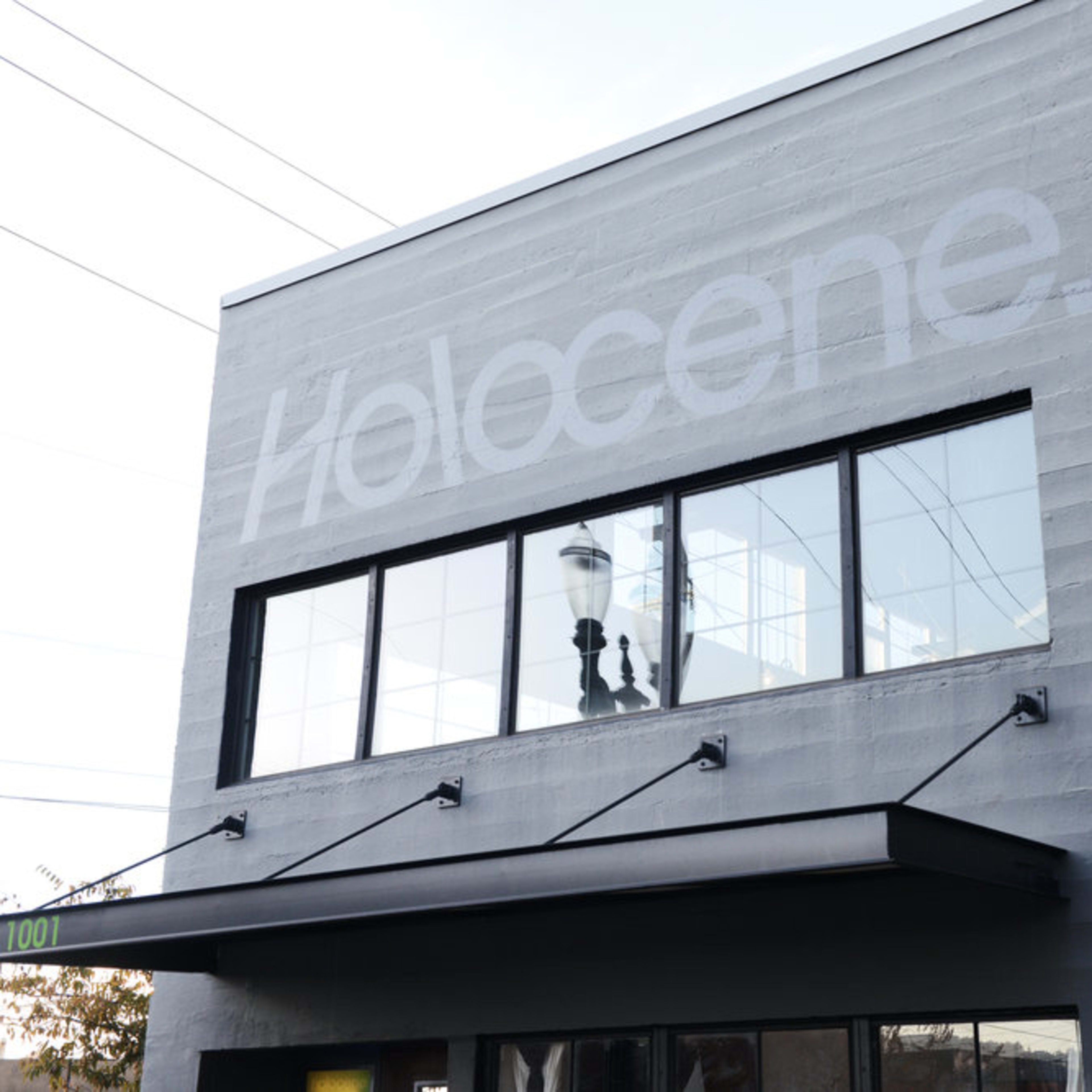 The exterior of a gray building features large windows and the word "Holocene" prominently displayed on the upper wall.