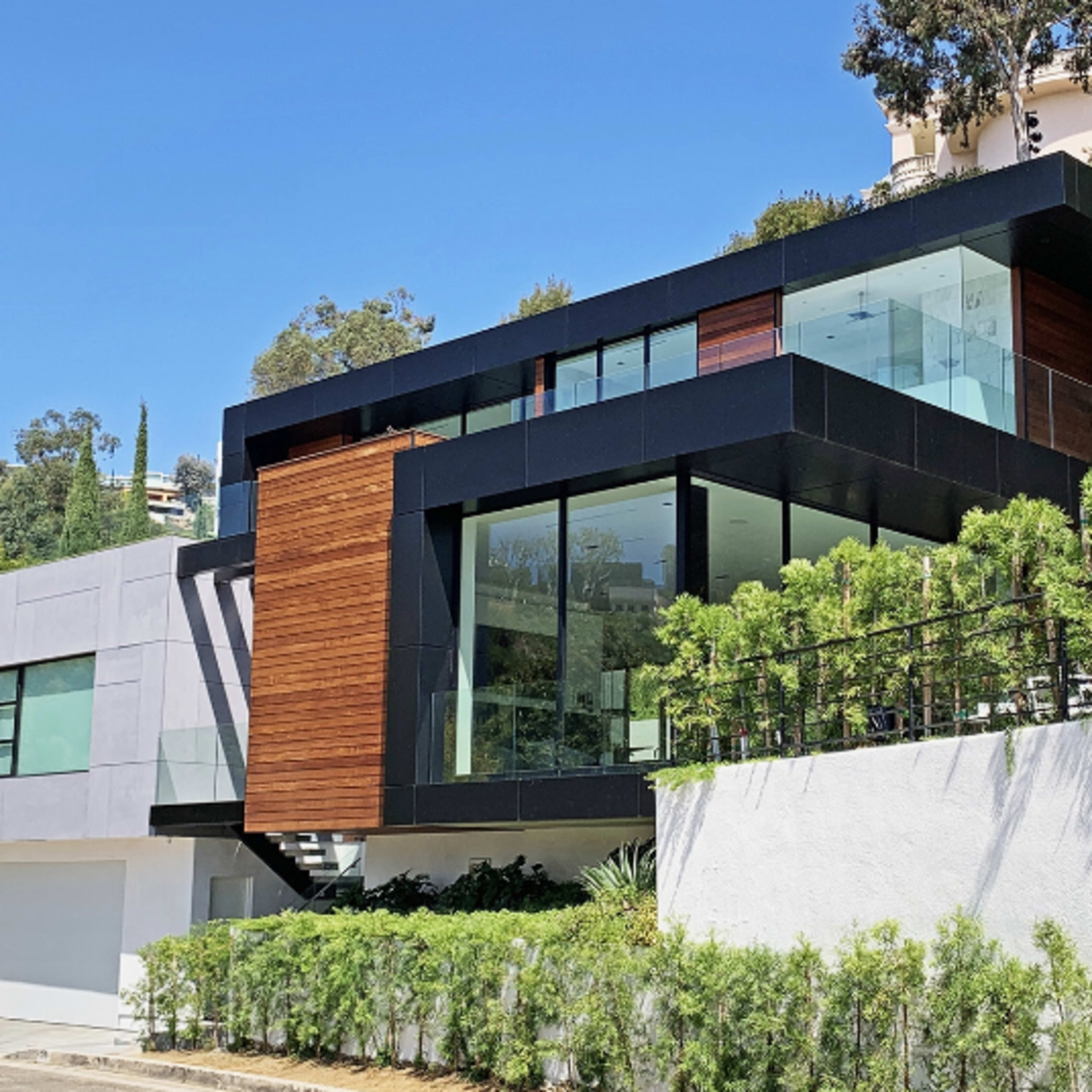 A contemporary two-story house featuring large glass windows, wooden accents, and a surrounding landscaped area.