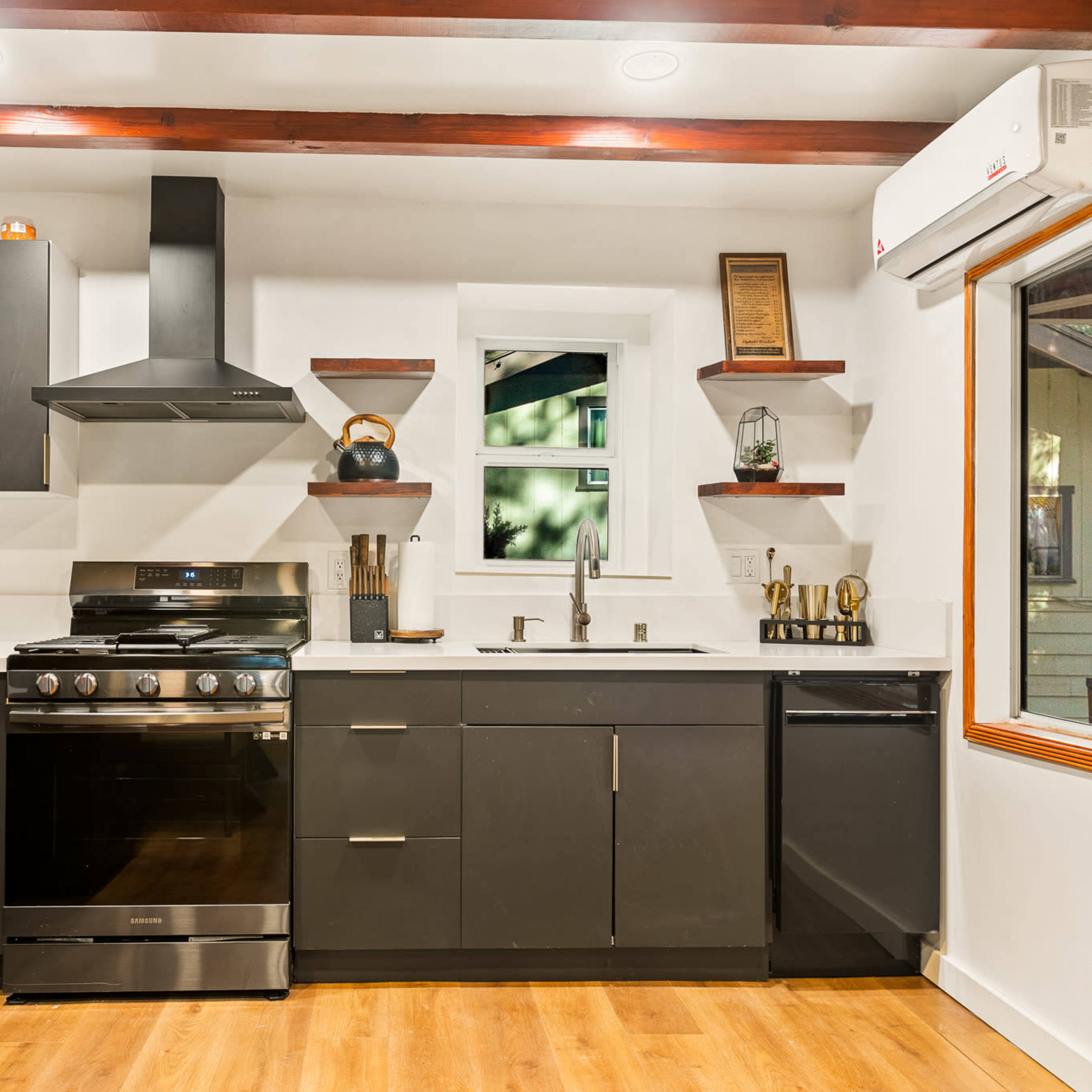 A modern kitchen featuring black cabinets, stainless steel appliances, and wooden beams along the ceiling.