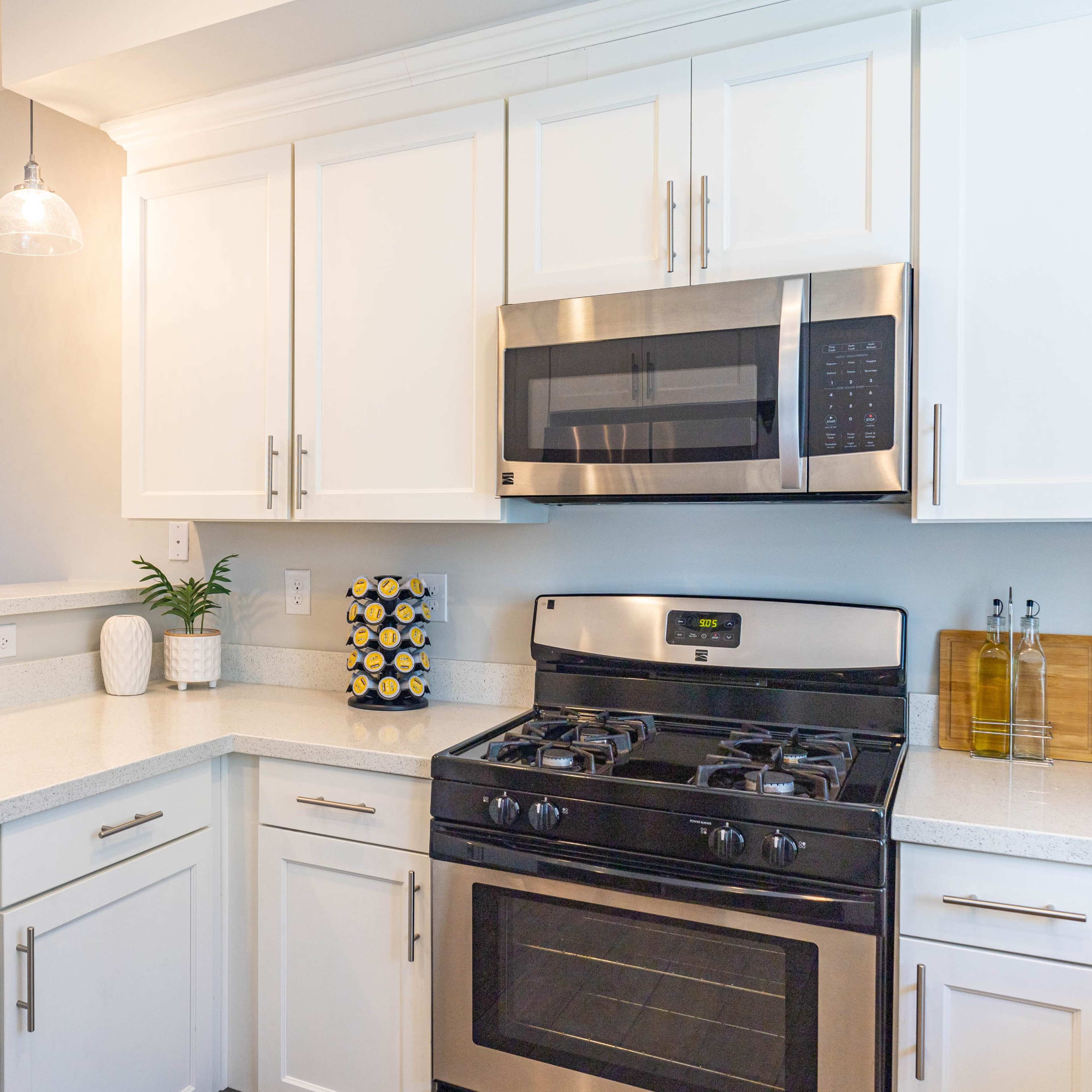 A modern kitchen featuring white cabinets, a stainless steel microwave and oven, and a light-colored countertop.