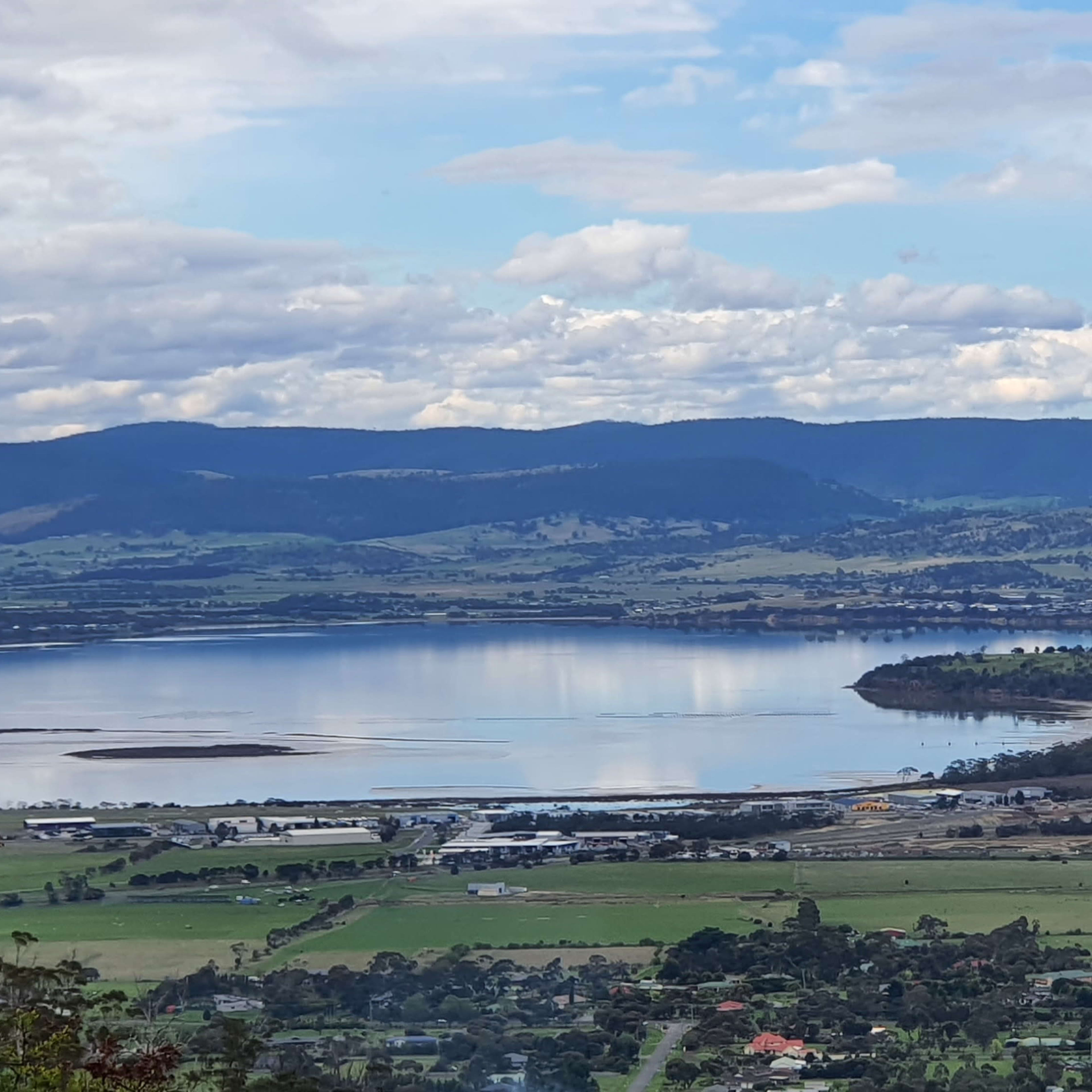 A landscape featuring a large lake surrounded by hills and farmland under a partly cloudy sky.