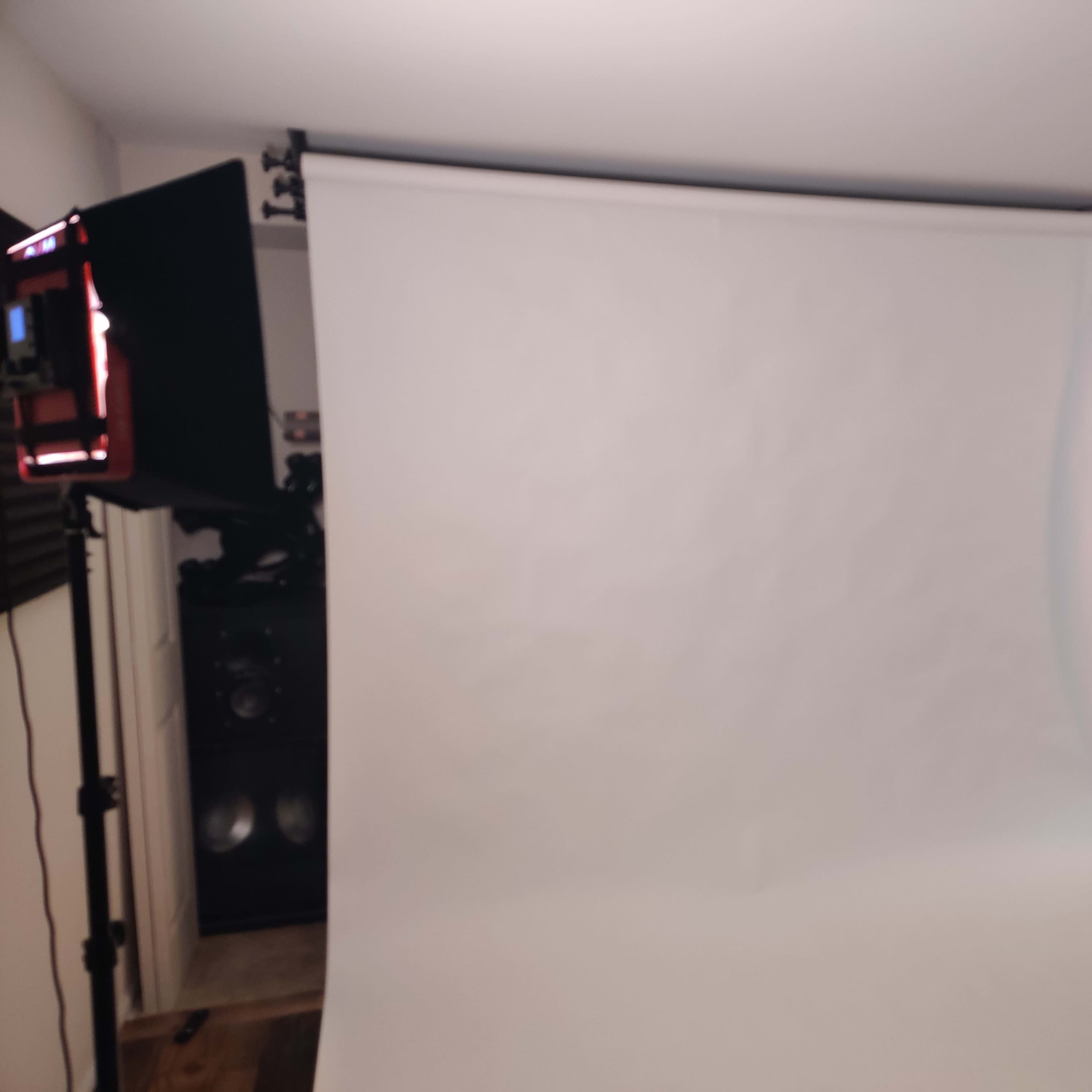 A blank white backdrop set up in a room with a small table, a television, and a light source on the side.
