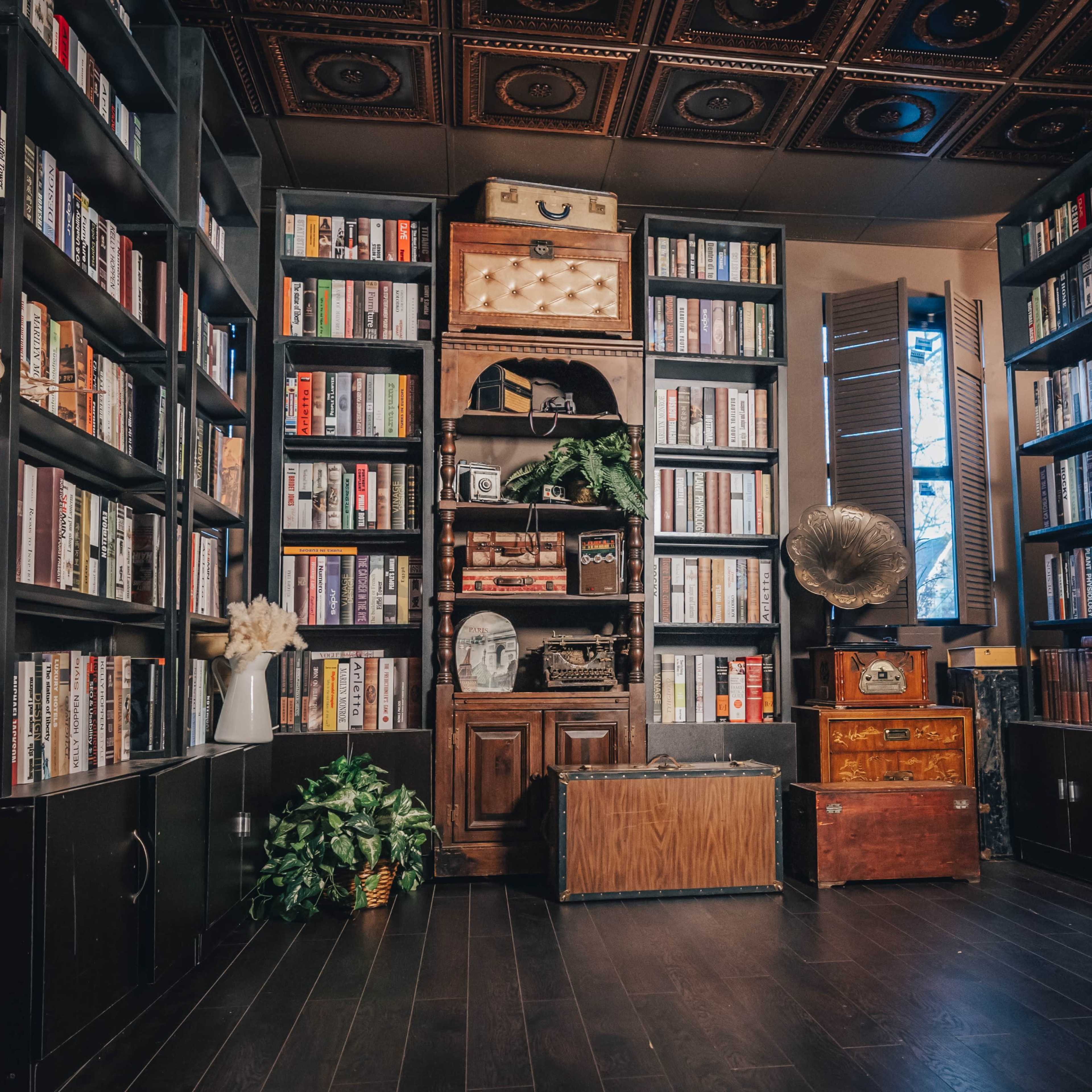 A cozy library with tall bookshelves filled with books, an antique gramophone, and various decorative items, all arranged around a wooden cabinet.