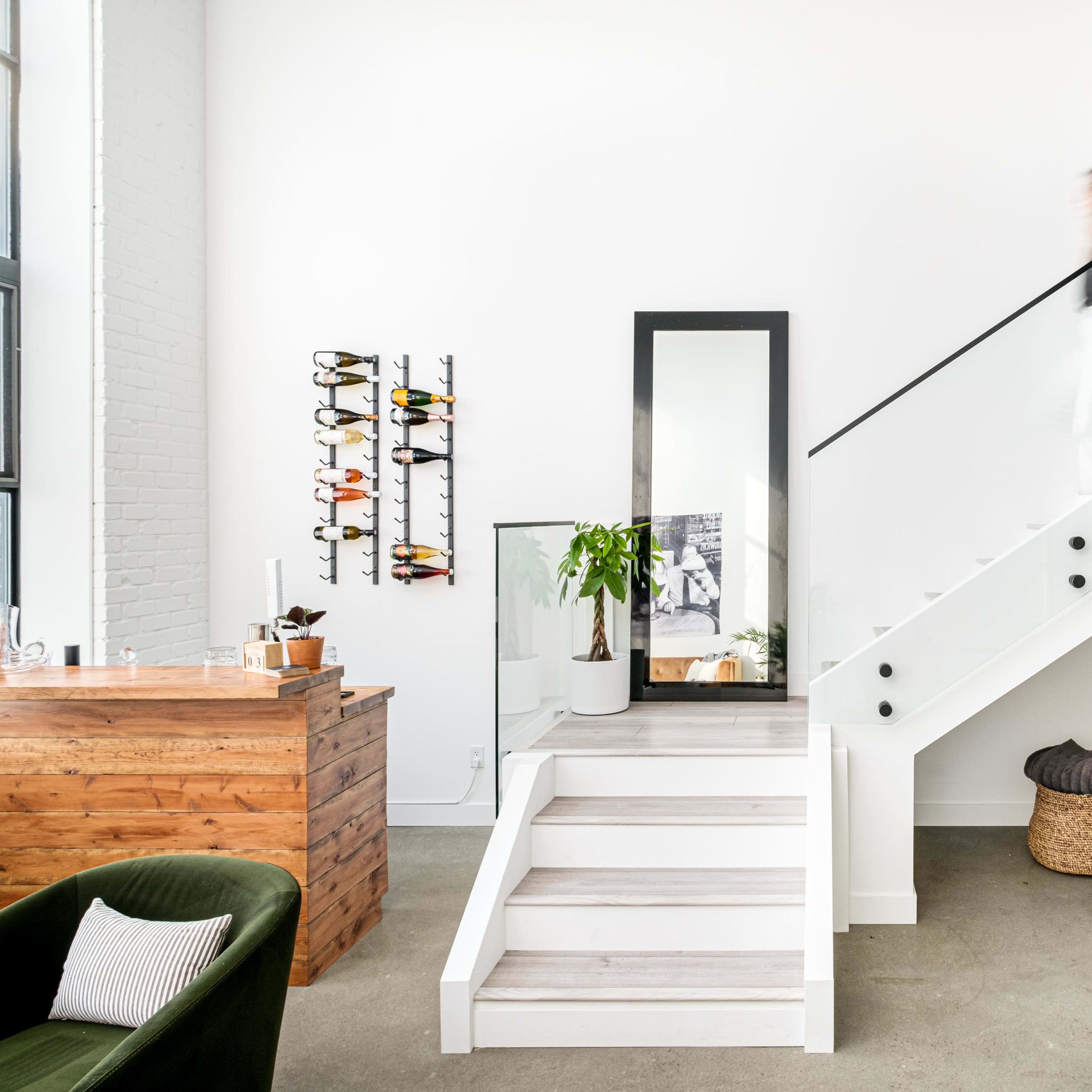 A woman walks up a staircase next to a living area featuring a sofa, a plant, and a wooden bar.