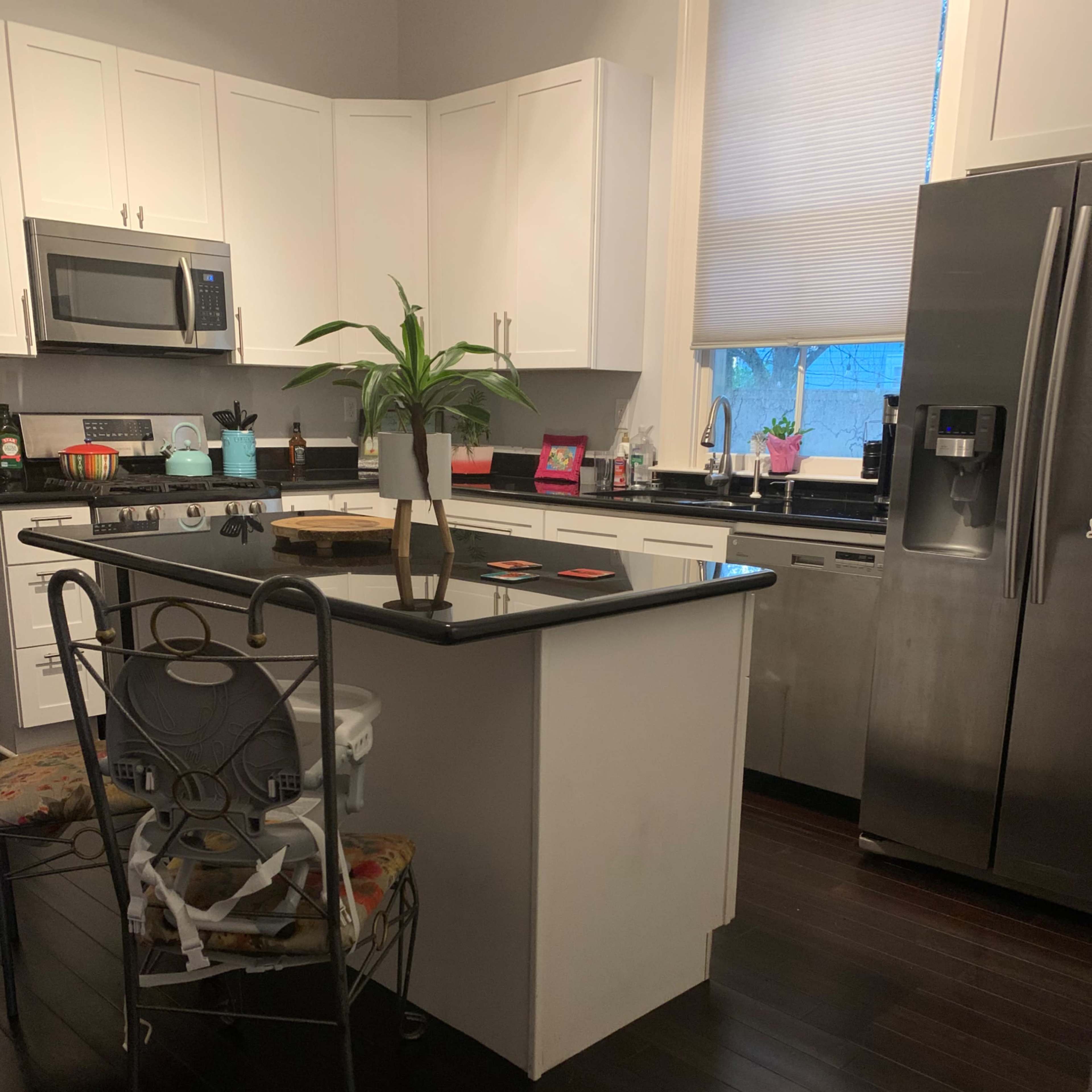 A modern kitchen features a central island with a plant, stainless steel appliances, and dark wooden flooring.