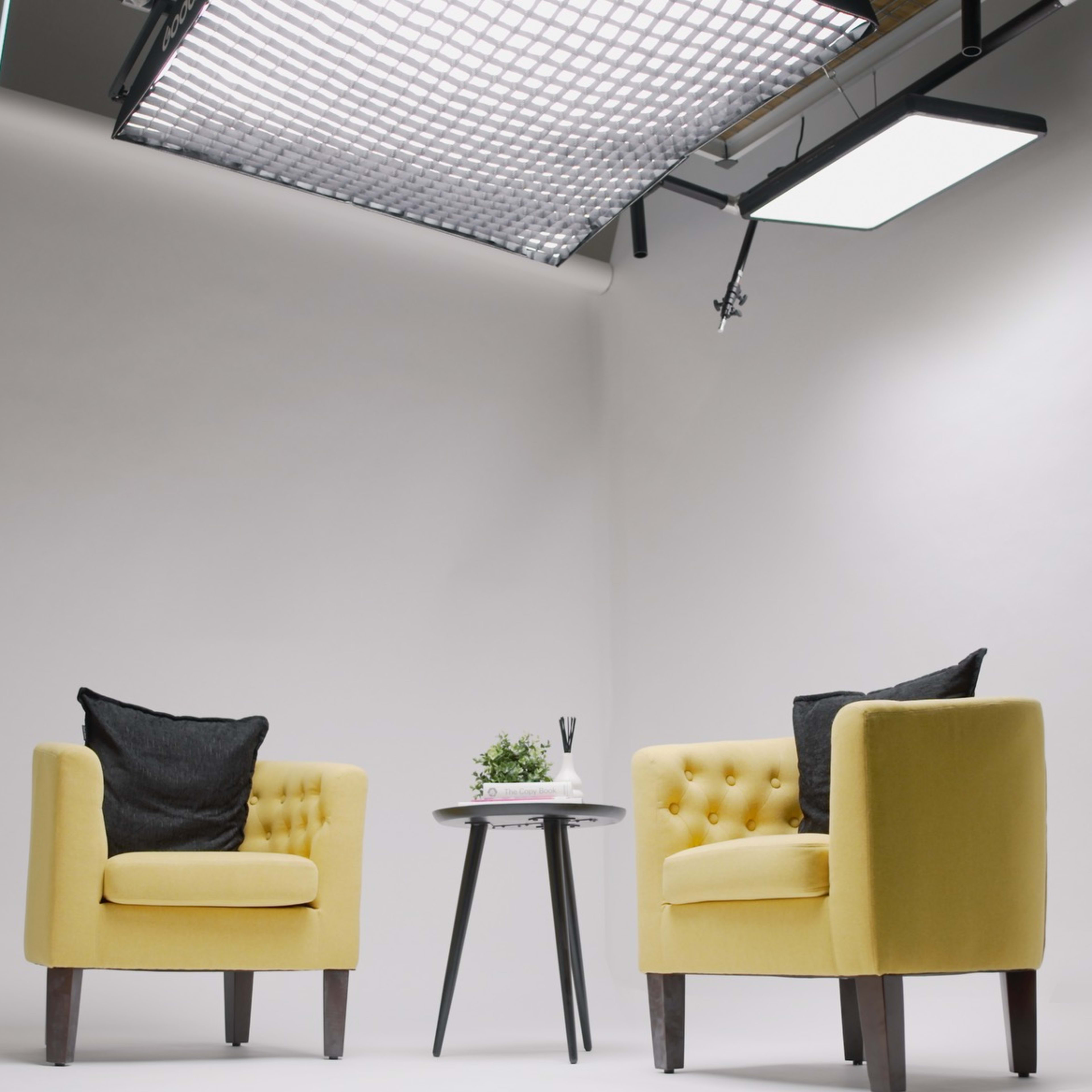 Two yellow chairs with black pillows facing each other across a small white table in a well-lit studio.