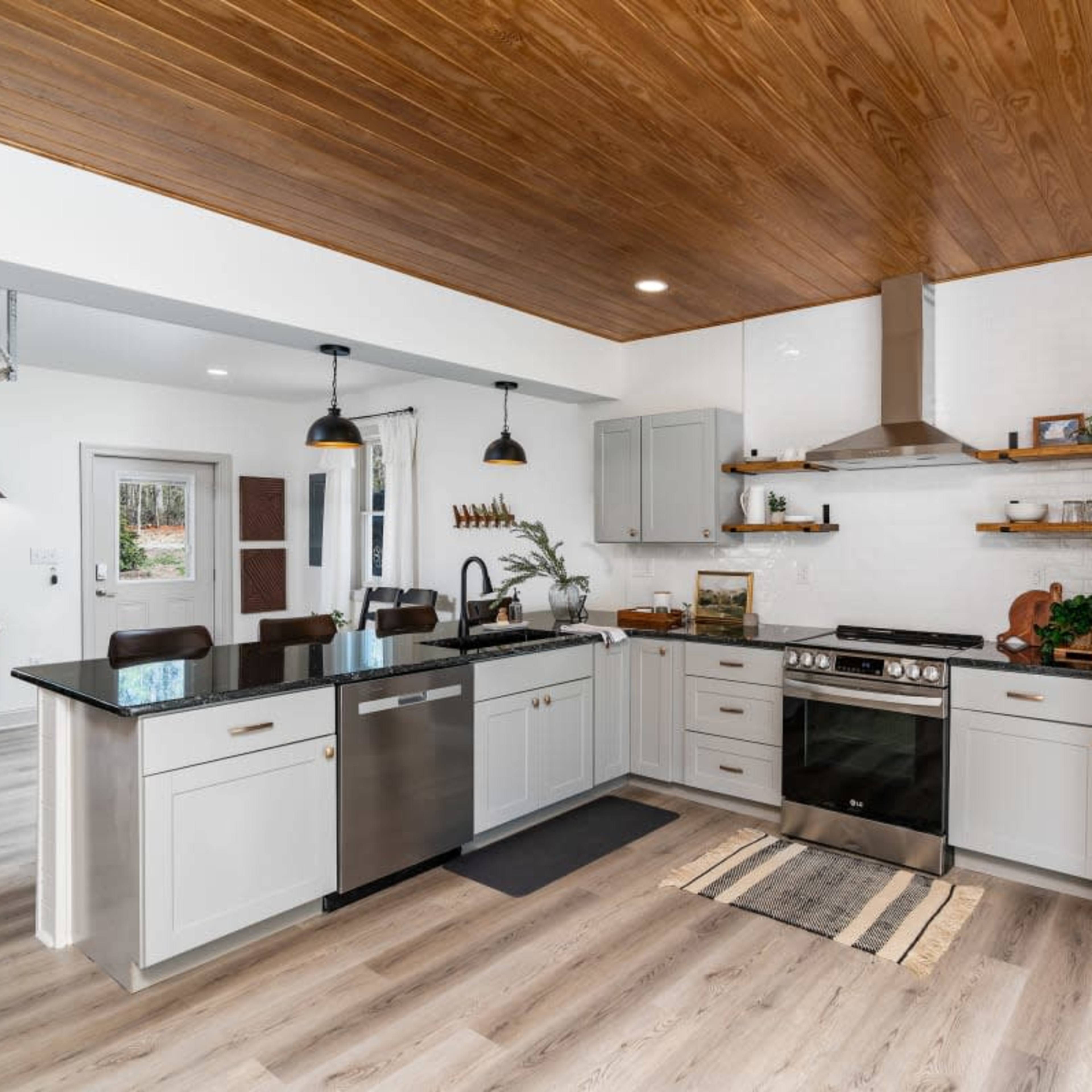 The kitchen features a modern design with stainless steel appliances, a central island, and wooden ceiling panels.