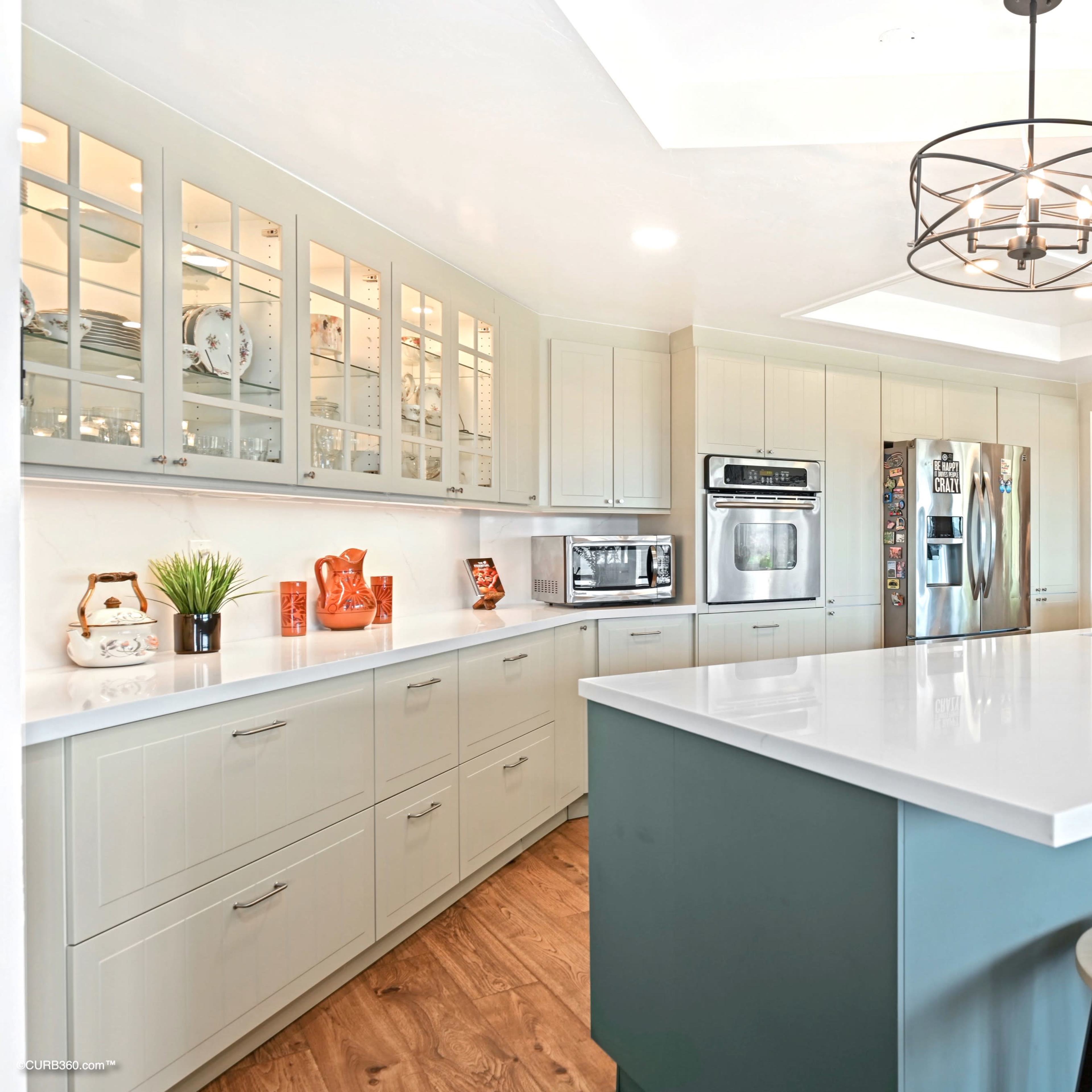 A modern kitchen with light cabinetry, a central island with seating, and a stainless steel refrigerator.