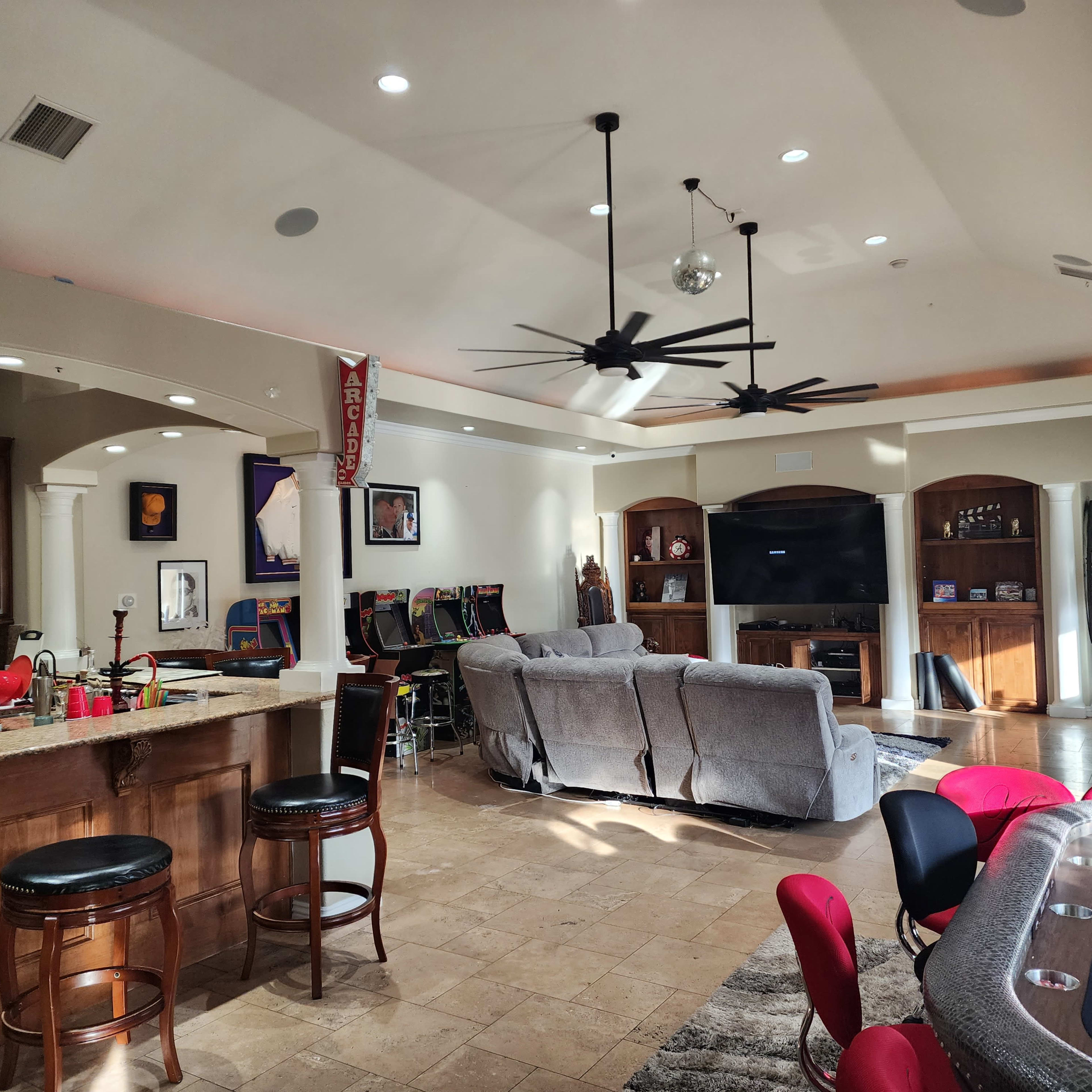 A spacious living area featuring a bar with stools, a poker table with red chairs, and a seating area with gray sofas.