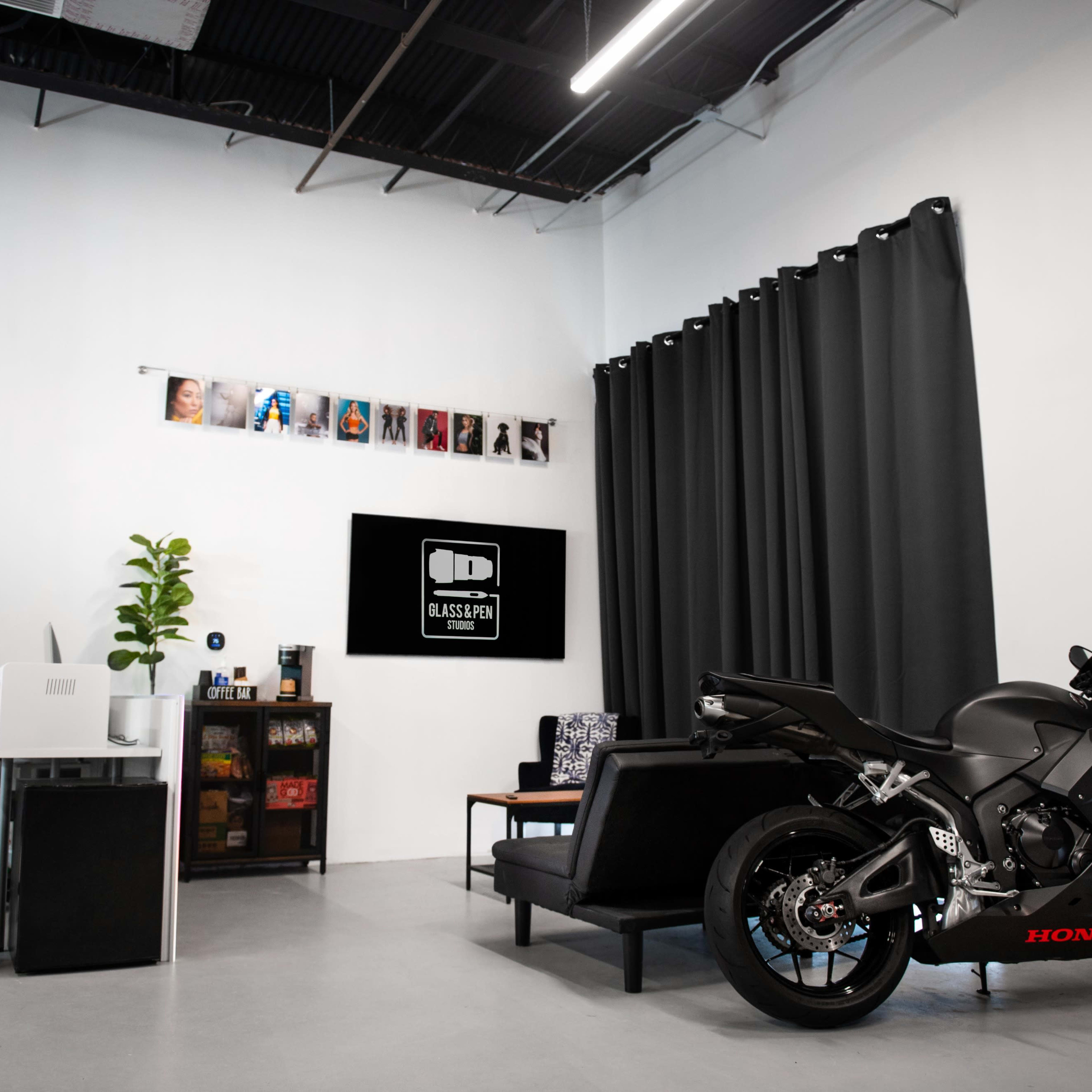 A sleek black motorcycle is parked beside a modern couch in a well-lit room featuring dark curtains and a television display.