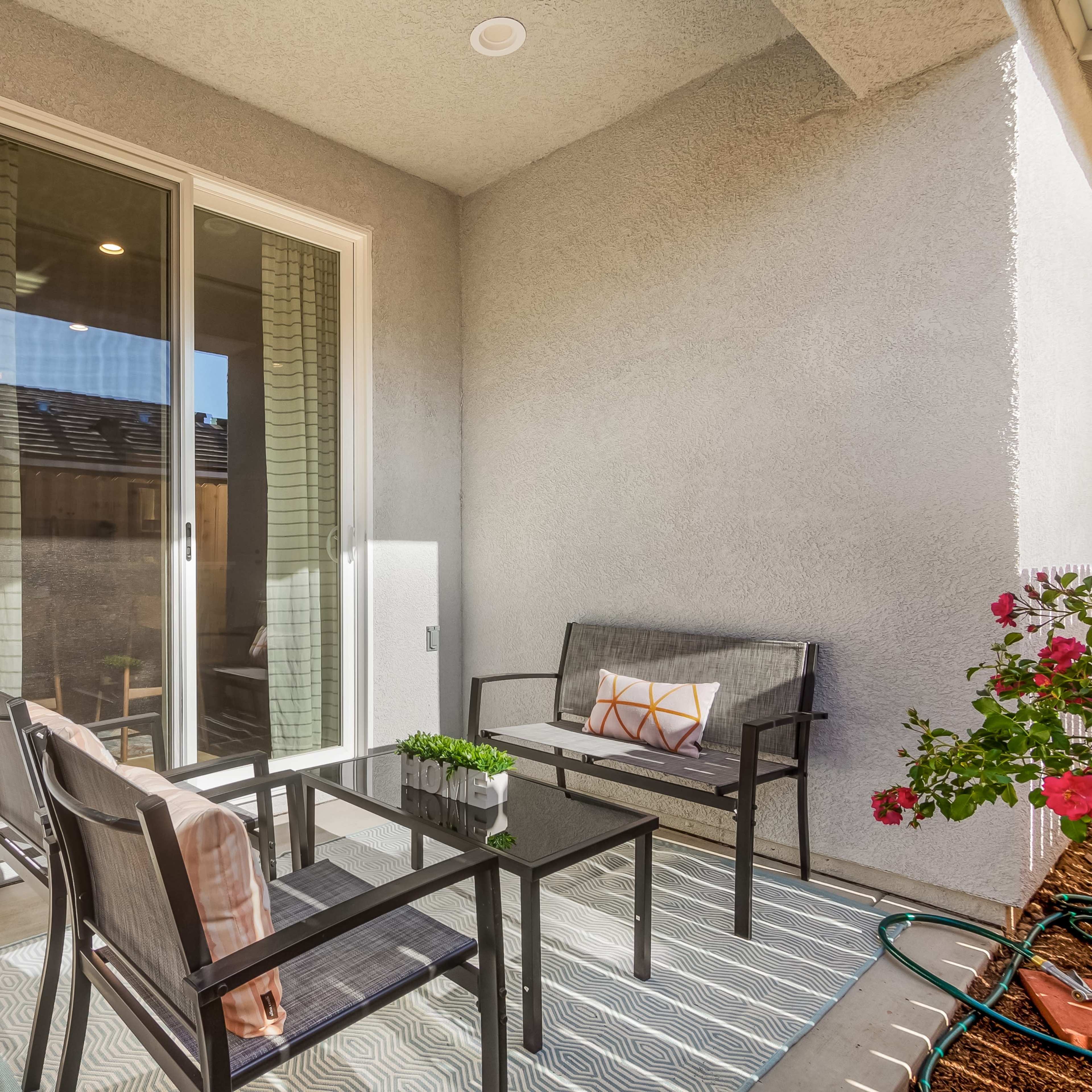 A small balcony features a seating area with two black chairs, a coffee table, and potted flowers nearby.