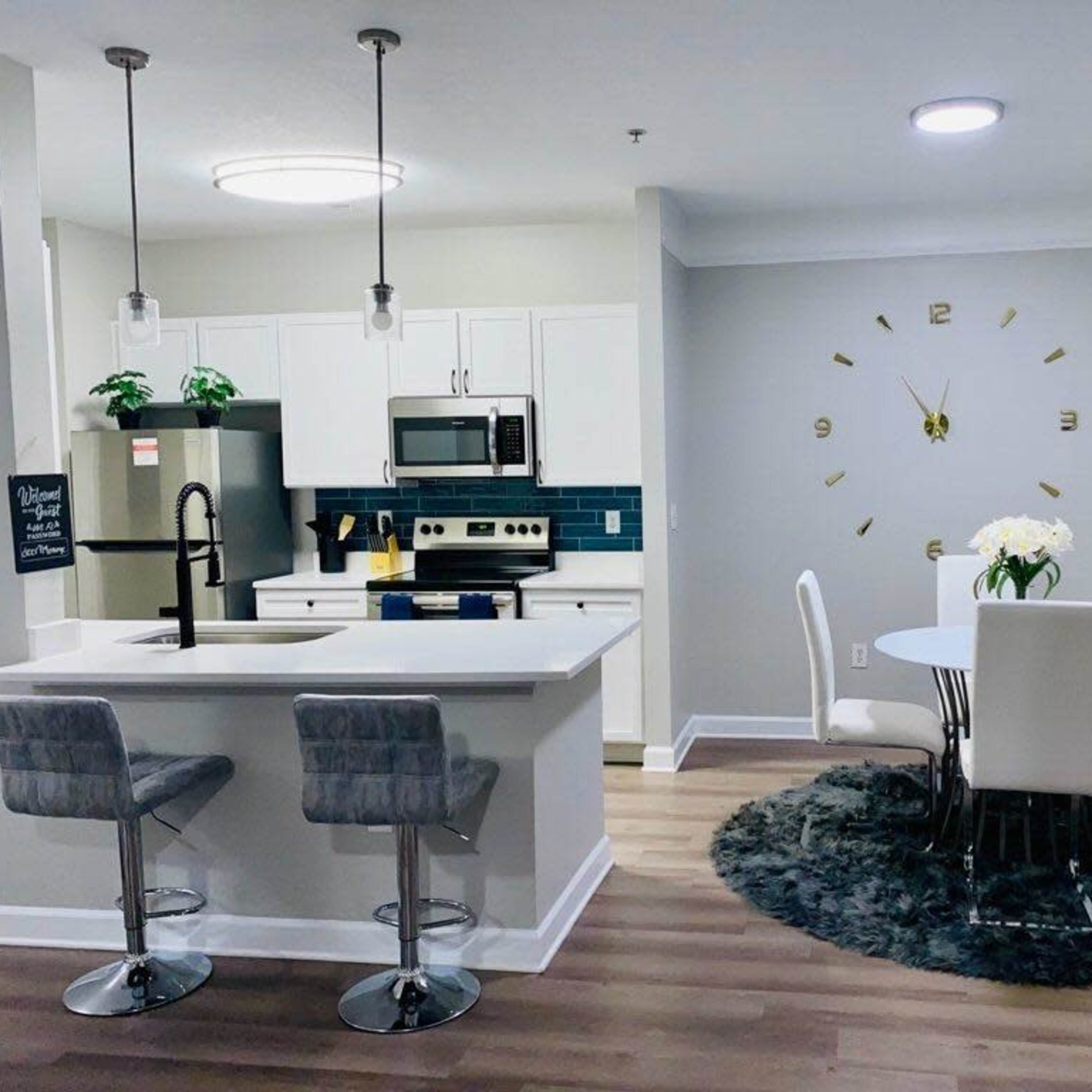 A modern kitchen and dining area featuring stainless steel appliances, a round dining table with white chairs, and a circular rug on a wooden floor.