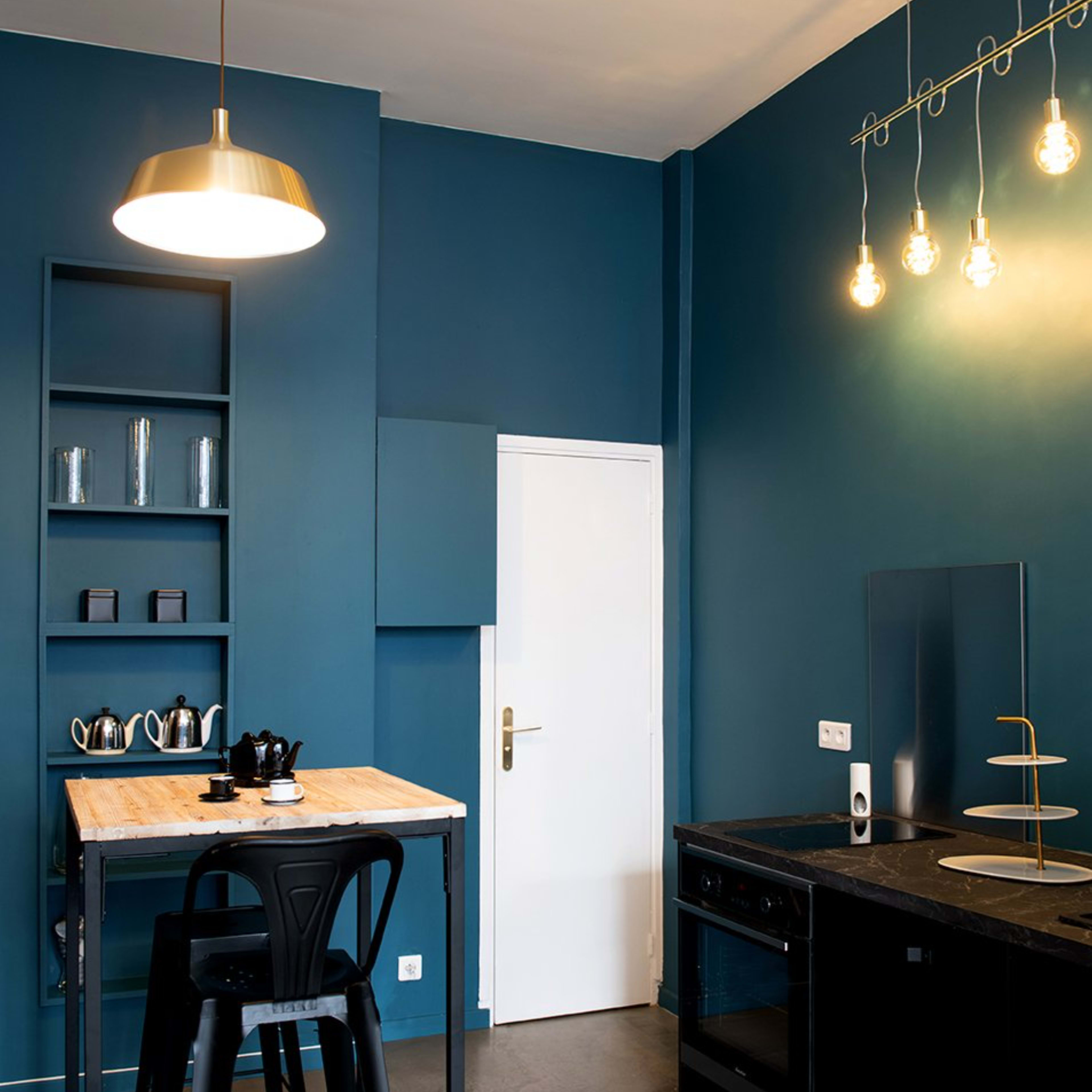 A modern kitchen with a blue wall, a wooden table with black stools, and sleek black cabinets and appliances.