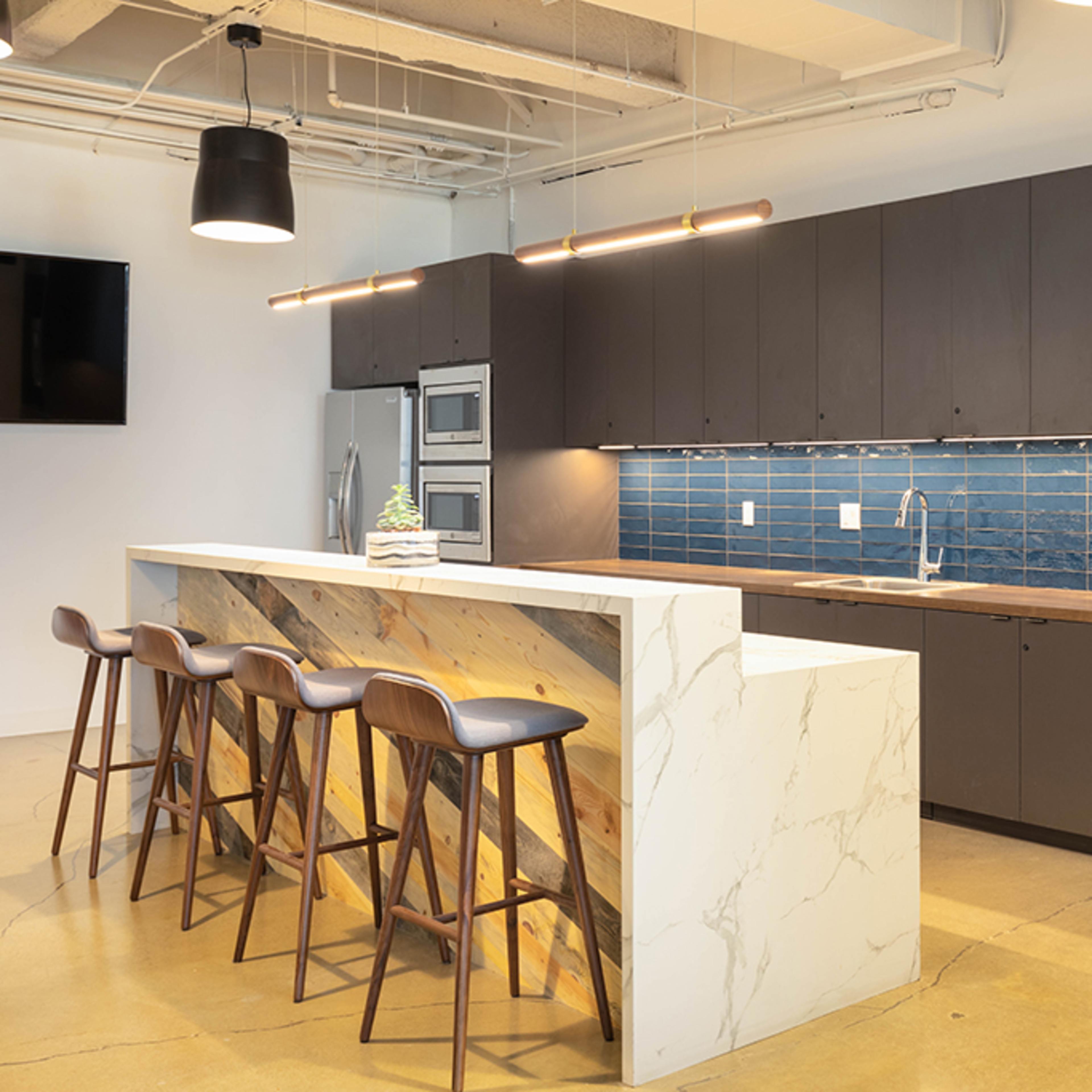 A modern kitchen with a marble-top island and dark cabinetry, featuring blue tiled backsplash and bar stools.