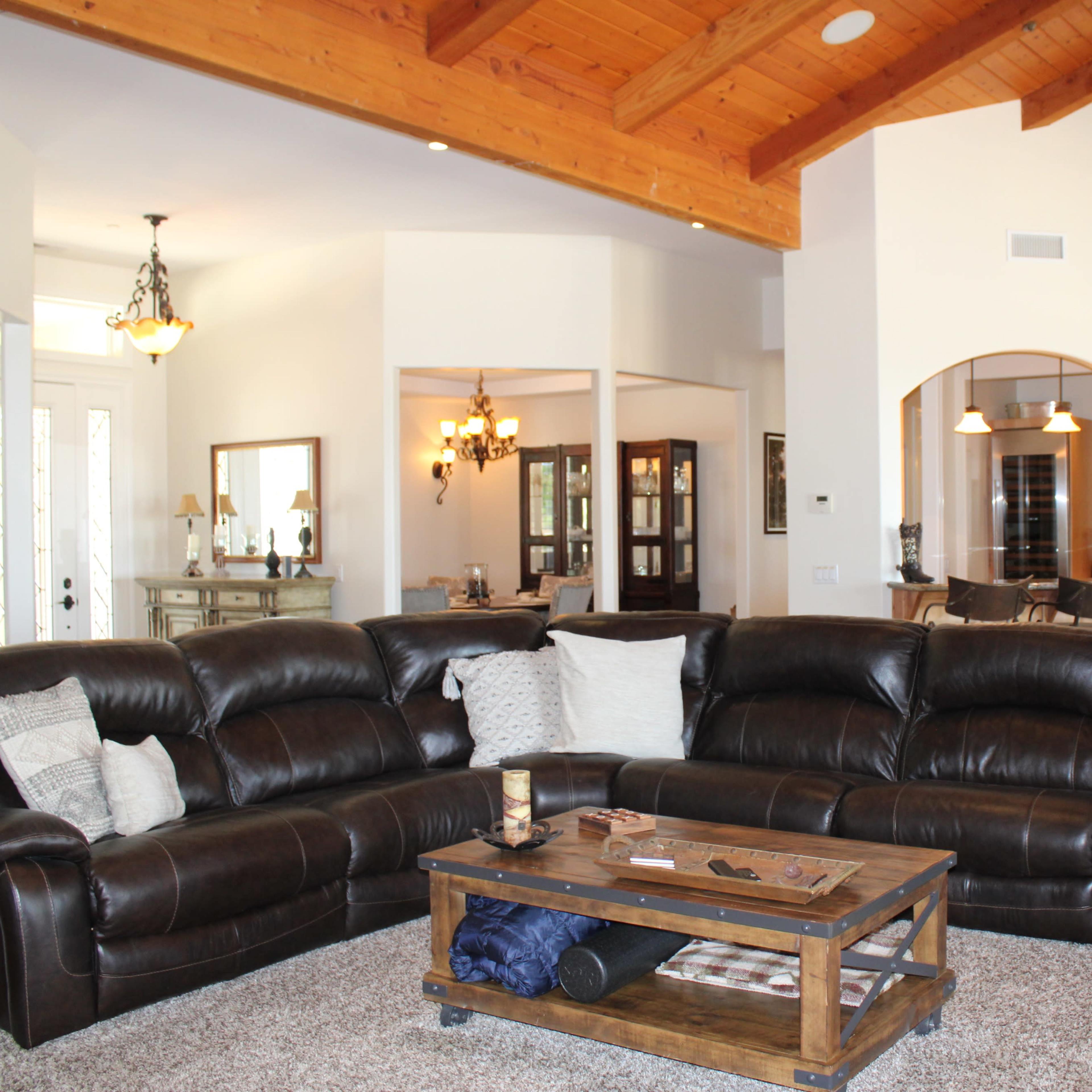 A spacious living area with a large brown sectional sofa, a wooden coffee table, and a view of a kitchen and dining area in the background.