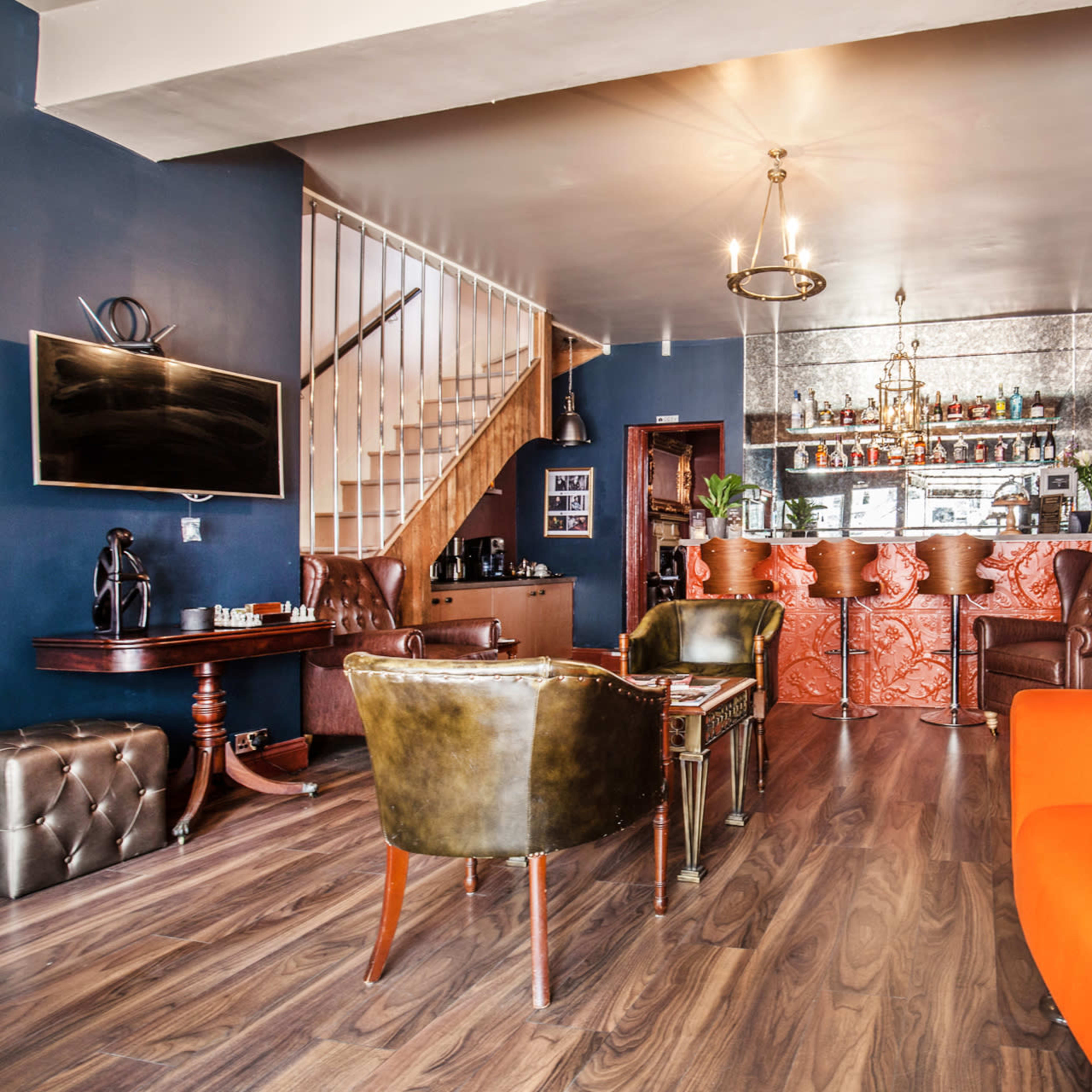 A modern interior with a seating area featuring an orange sofa, a brown leather chair, and a bar counter in the background.