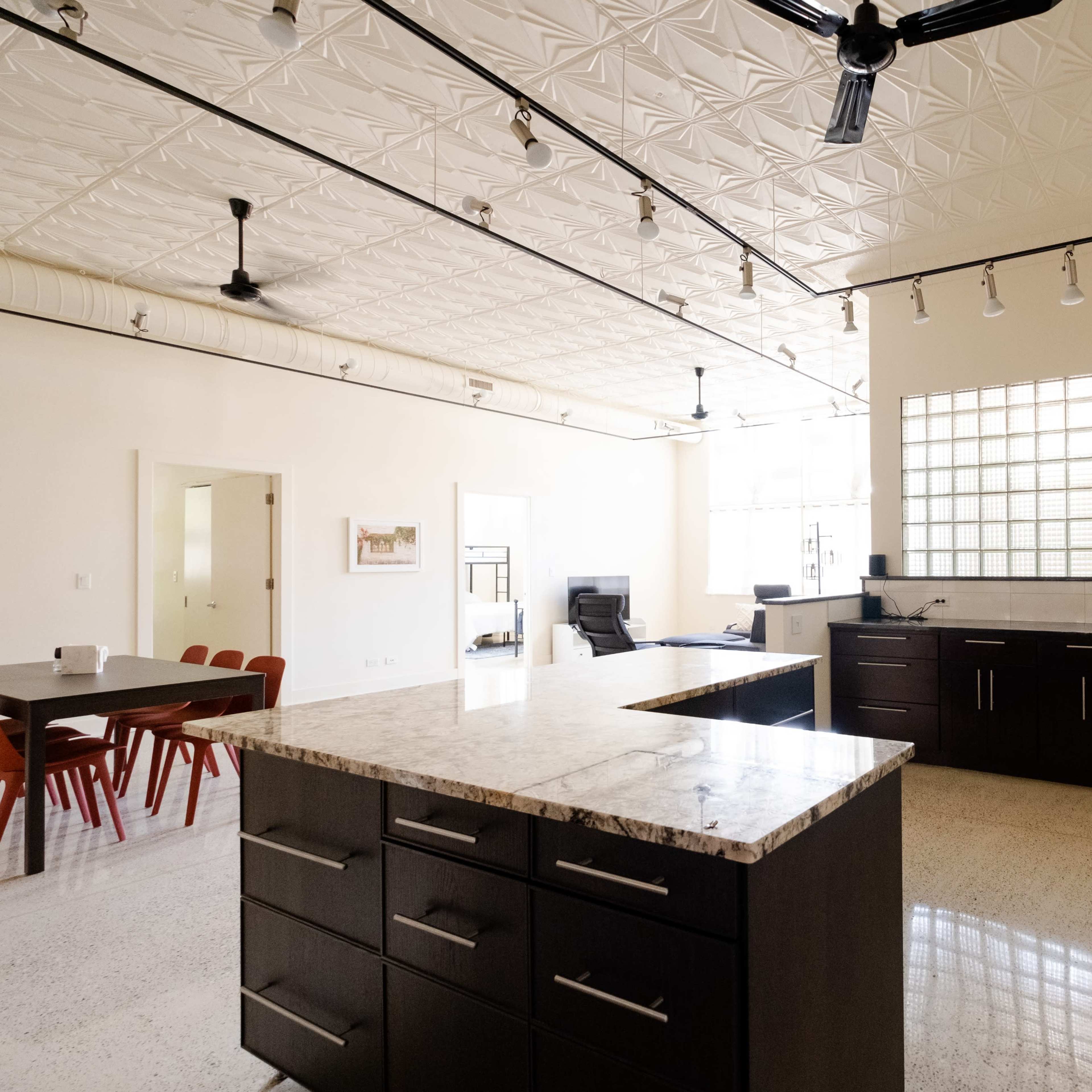 A modern kitchen with dark cabinetry, a large island with a granite countertop, and a geometric ceiling design, illuminated by overhead lights.