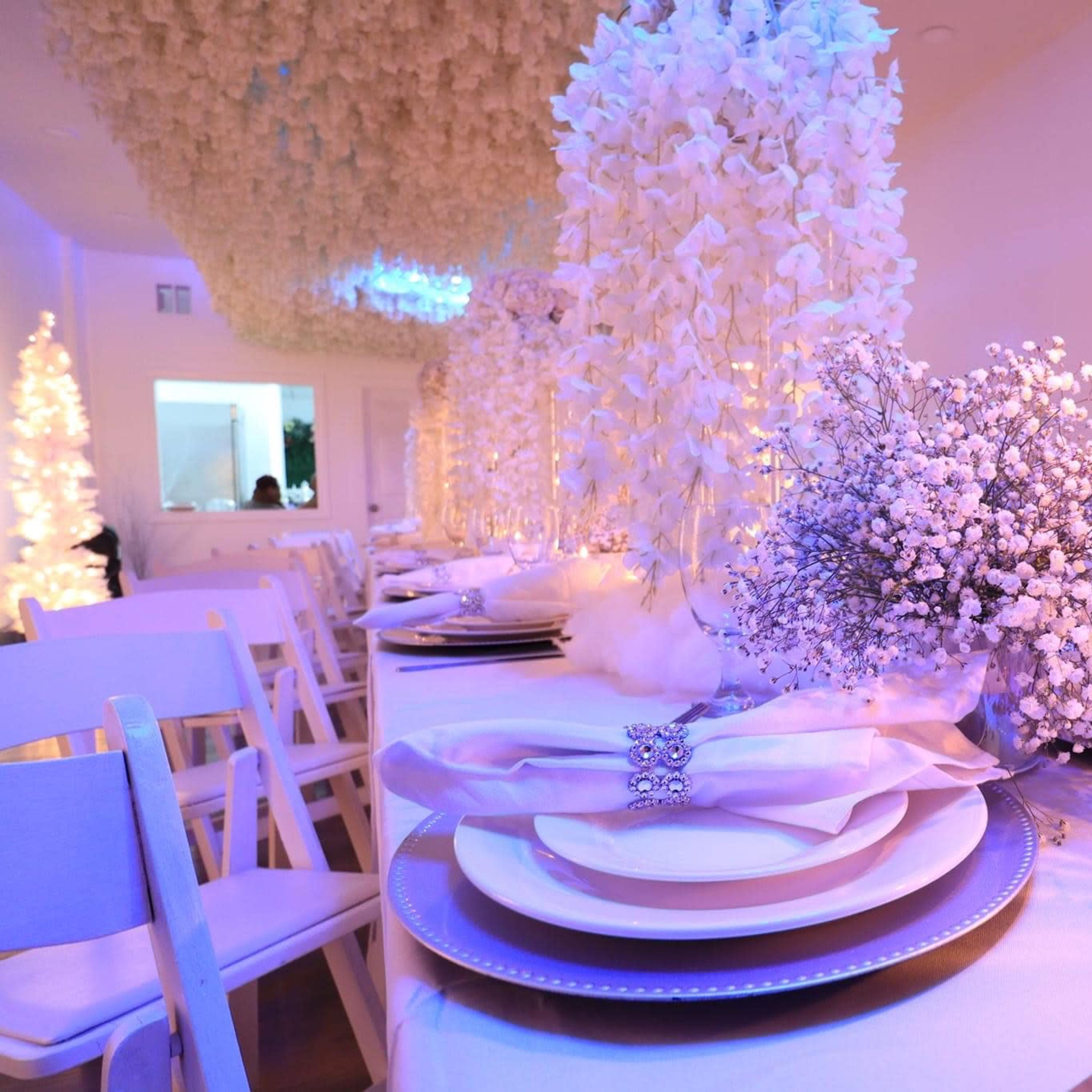 A elegantly arranged dining table set with white plates, fresh flowers, candles, and soft lighting in a decorated indoor space.