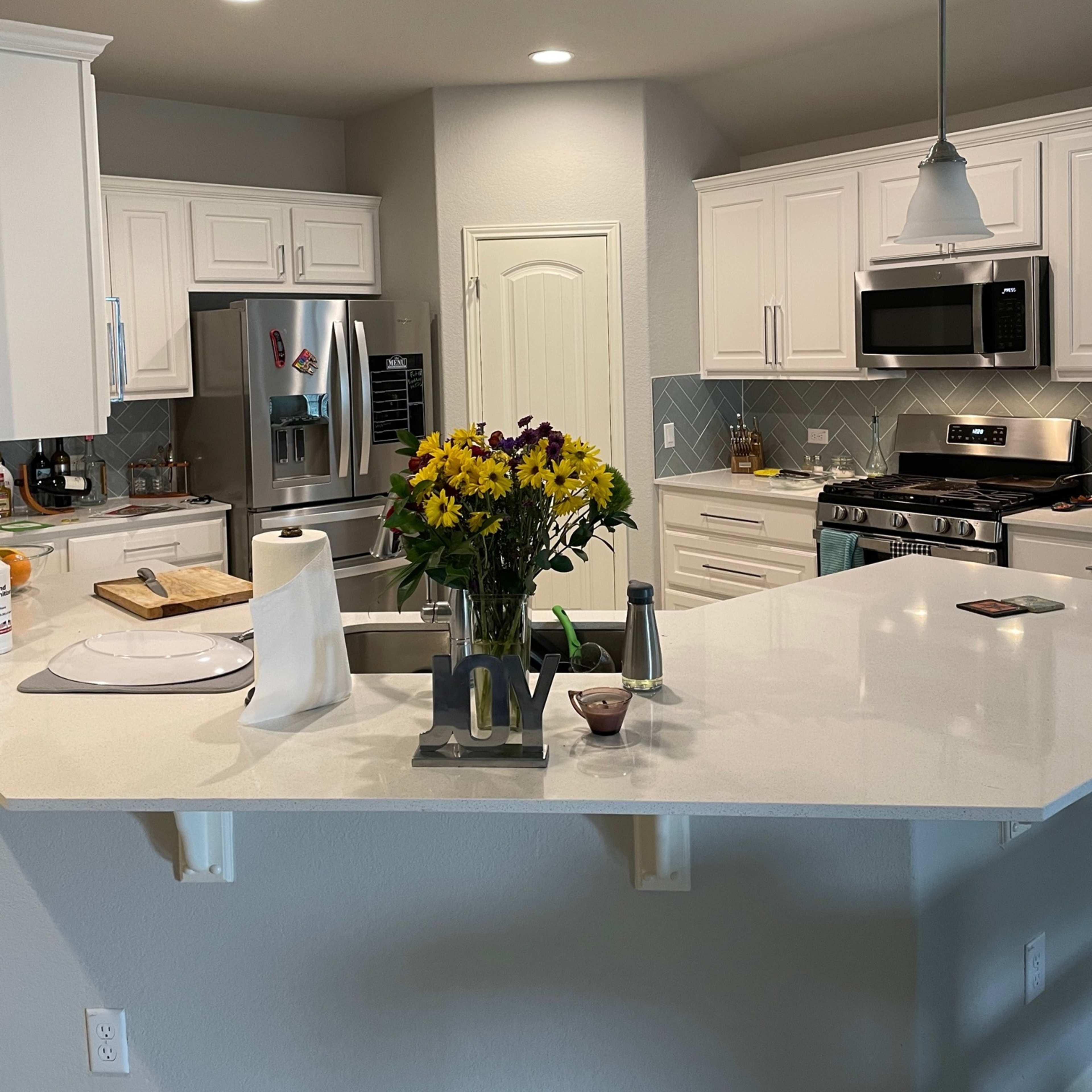 A modern kitchen features white cabinets, stainless steel appliances, and a center island with a bouquet of flowers.