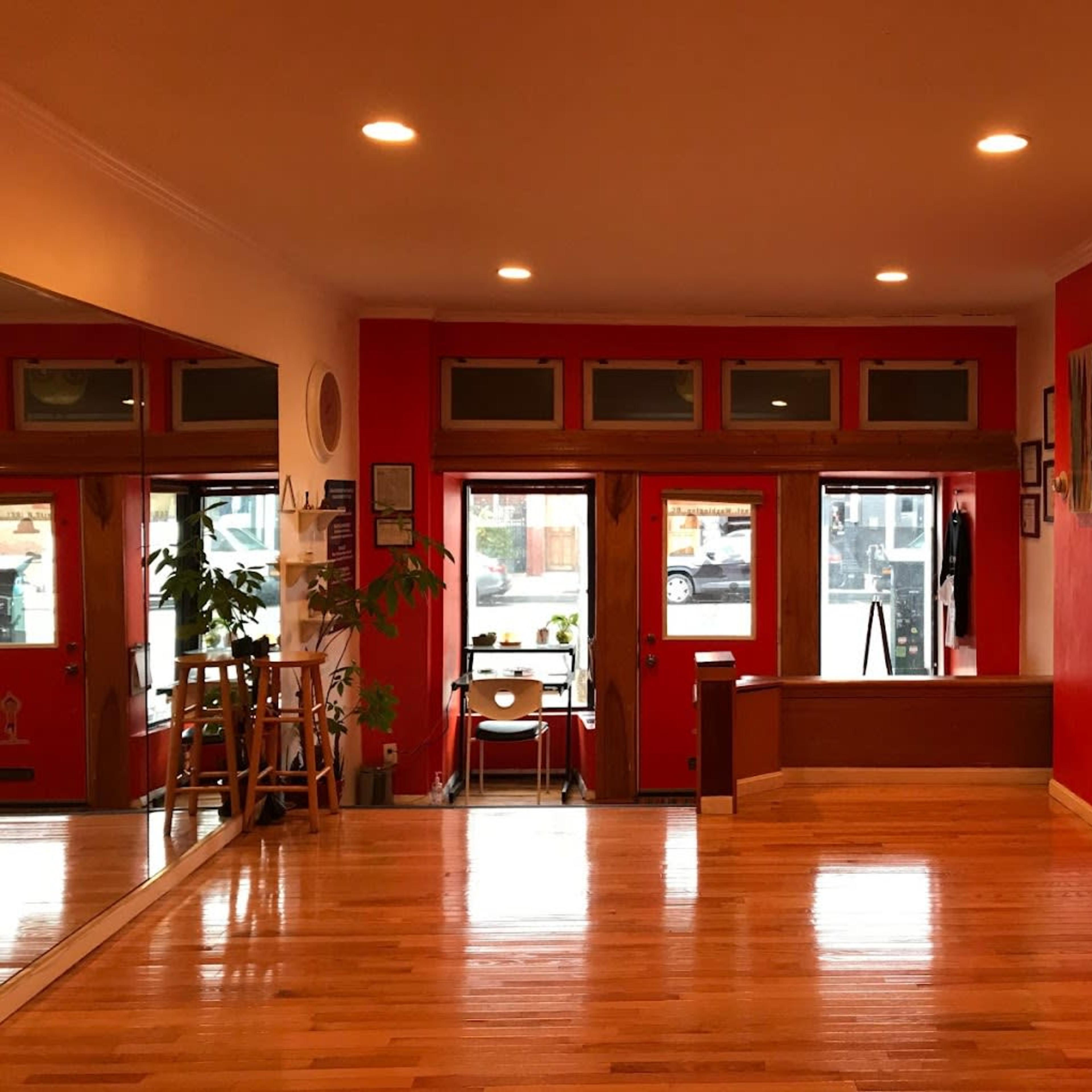A spacious room with wooden floors, red walls, and large windows that allow natural light to enter.