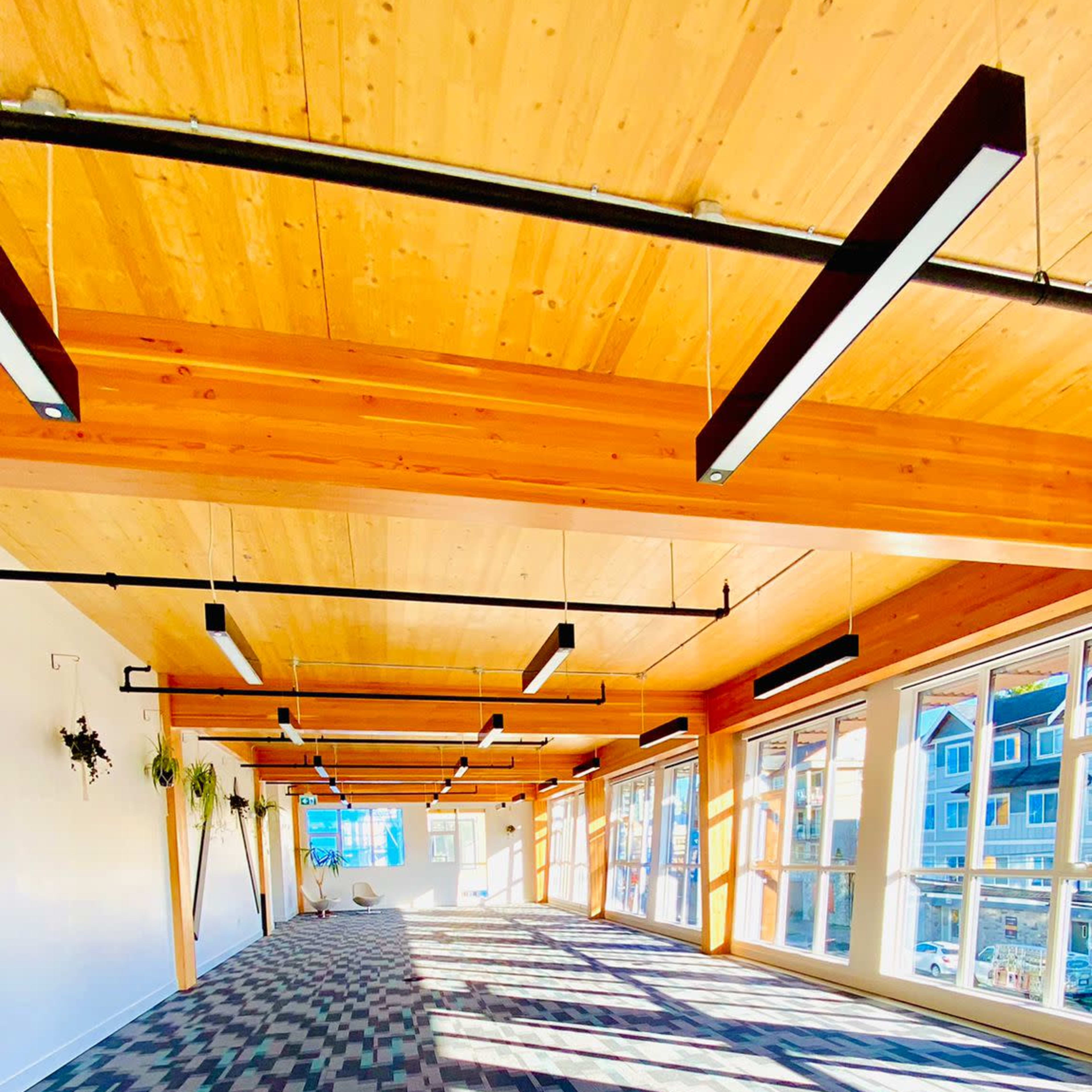 A spacious interior with wooden beams and a patterned carpet, illuminated by natural light streaming through large windows.