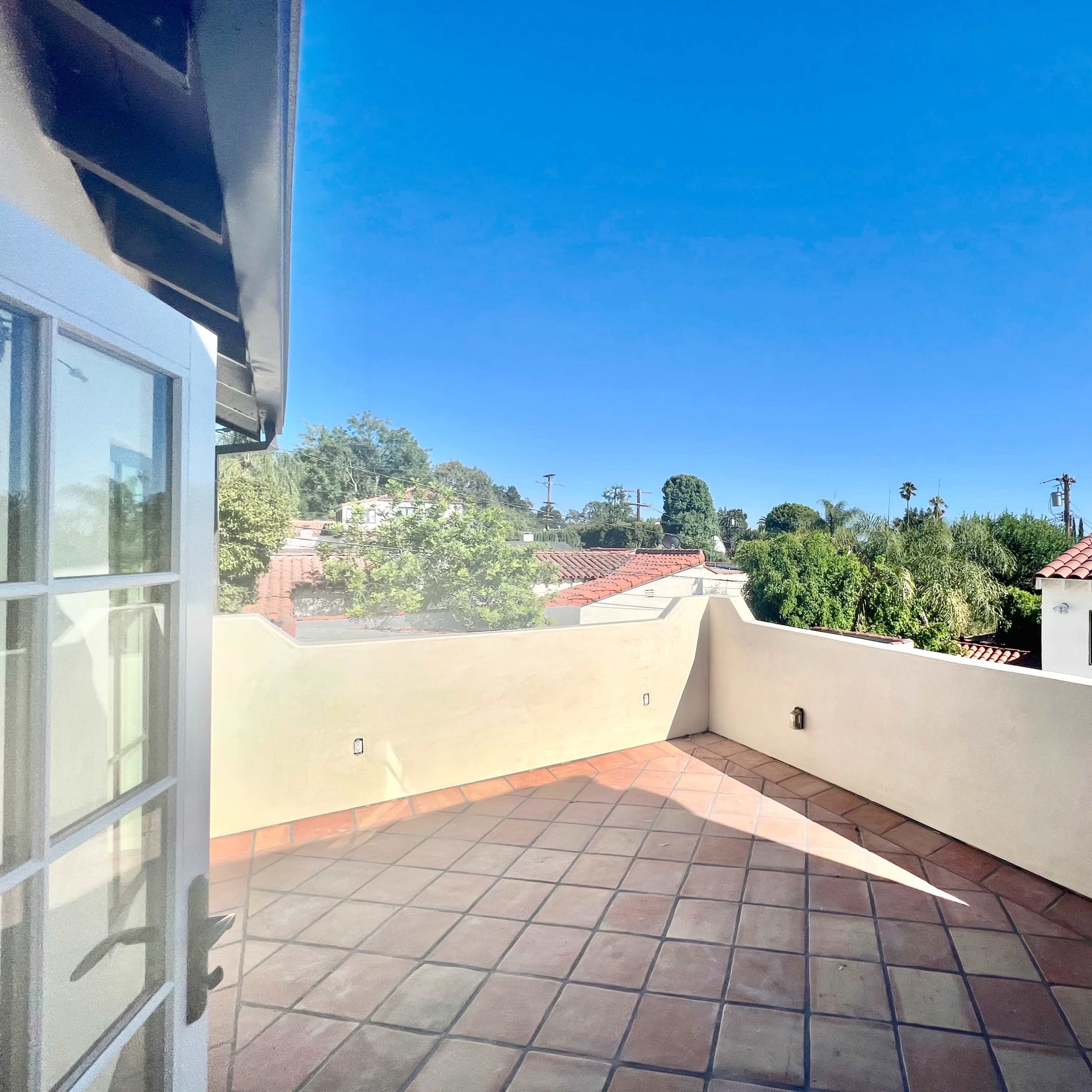 A tiled rooftop terrace with a clear blue sky and adjacent rooftops in the background.