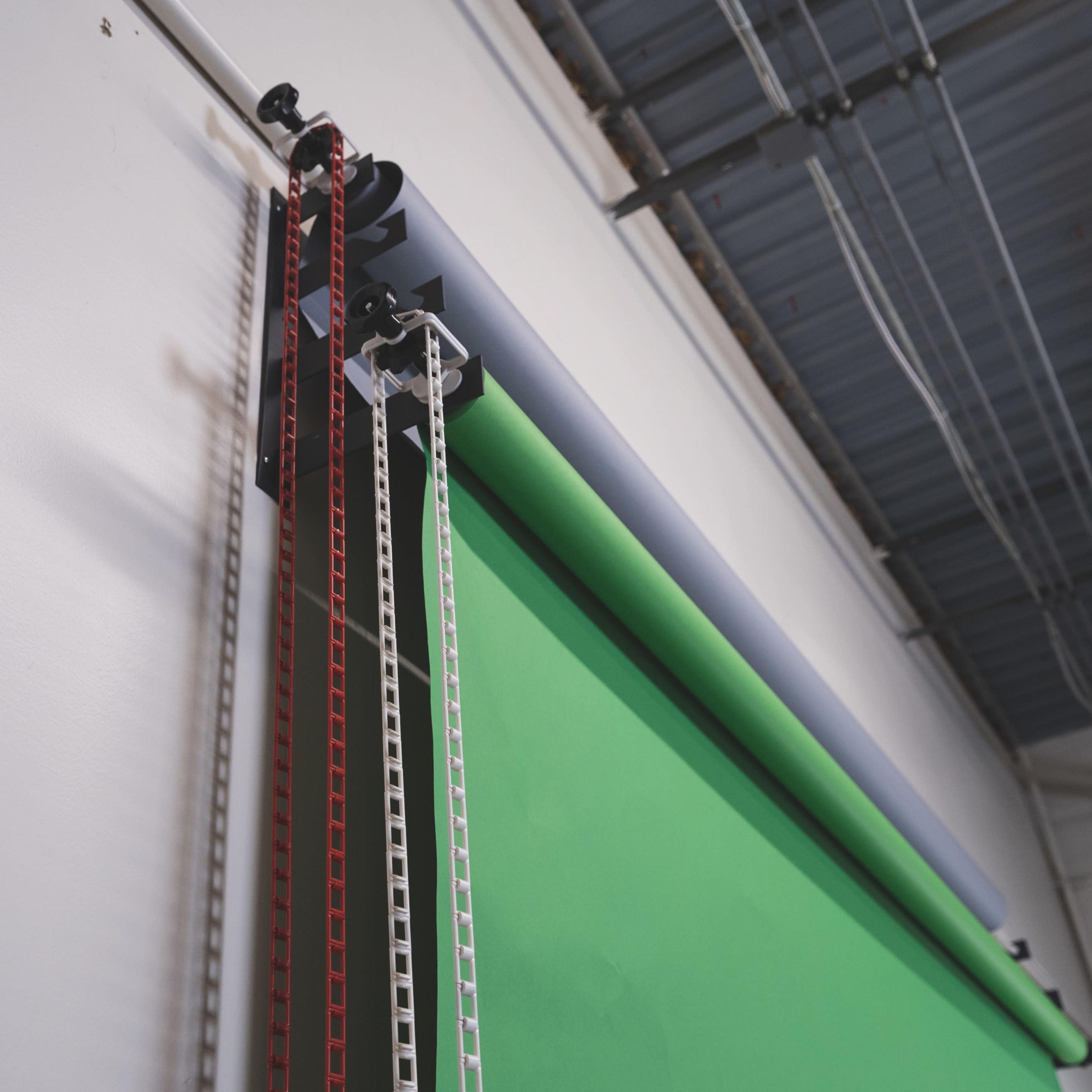 A green screen setup with paper rolls mounted on a wall beneath an industrial ceiling.