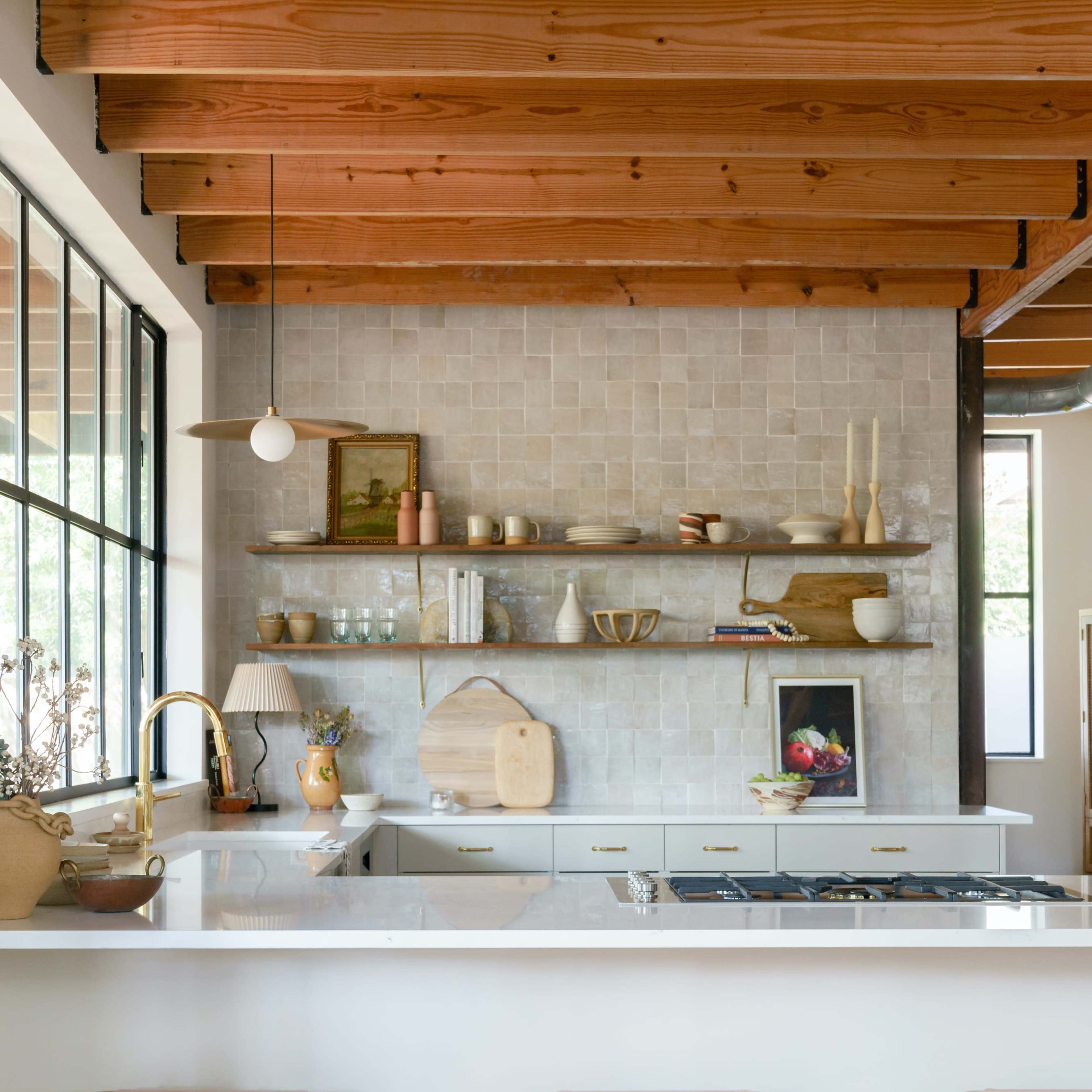 A modern kitchen with wooden beams, a white countertop, three bar stools, and open shelving displaying various kitchenware and decor.