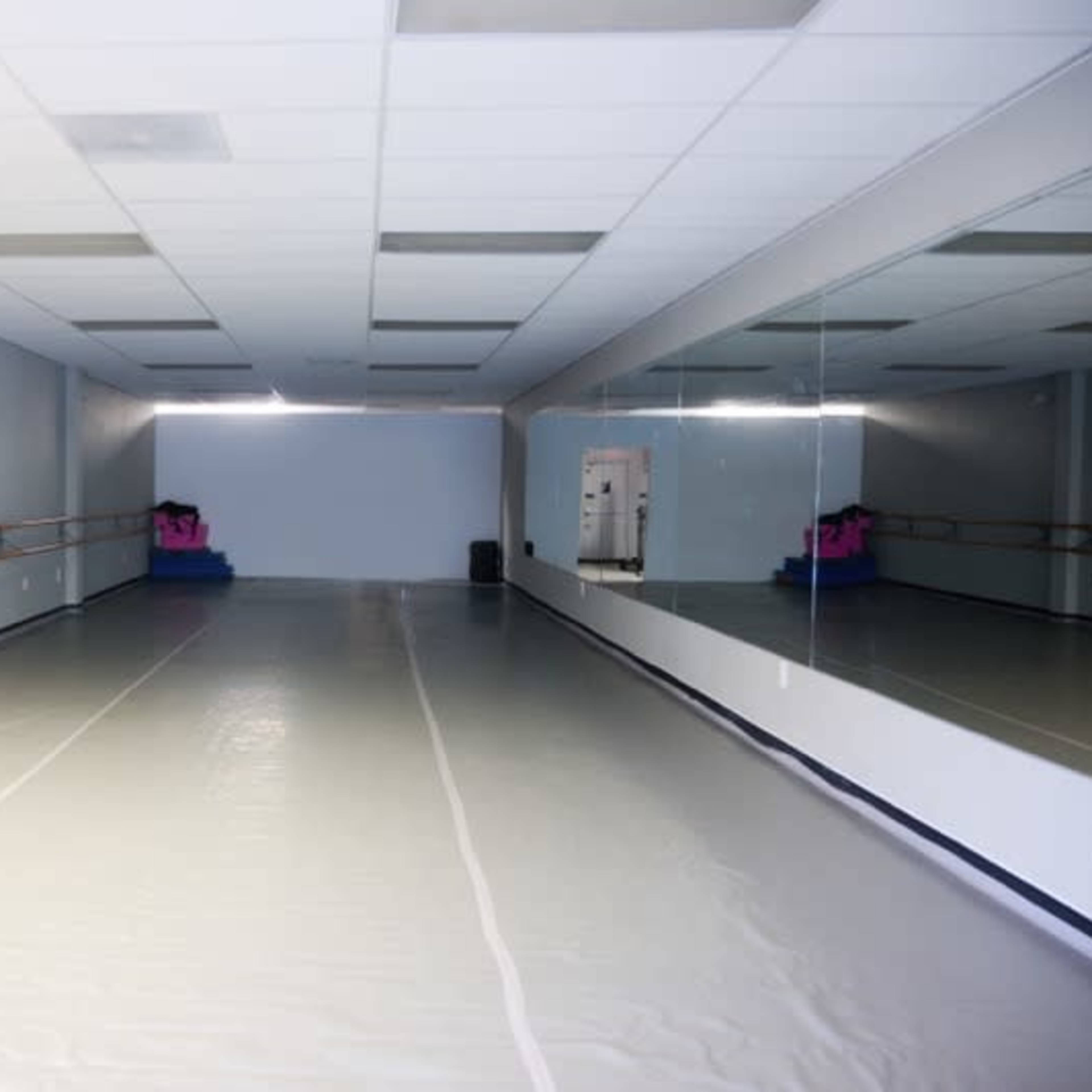 A spacious dance studio with mirrored walls and a smooth floor, illuminated by overhead lights.