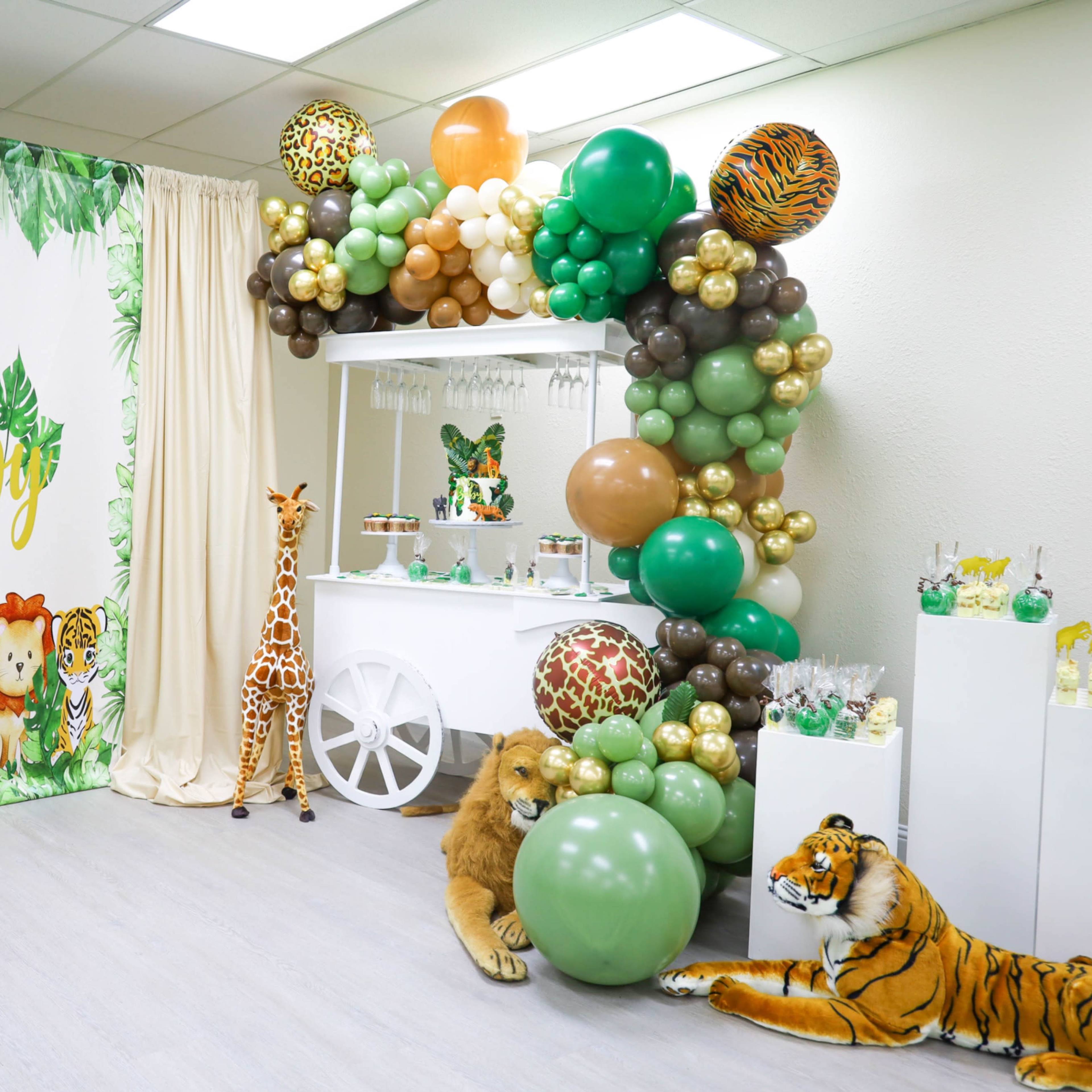 The scene features a decorated room for a baby shower, with a green and animal-themed backdrop, a balloon arch, and stuffed animal decorations including a lion and a tiger.