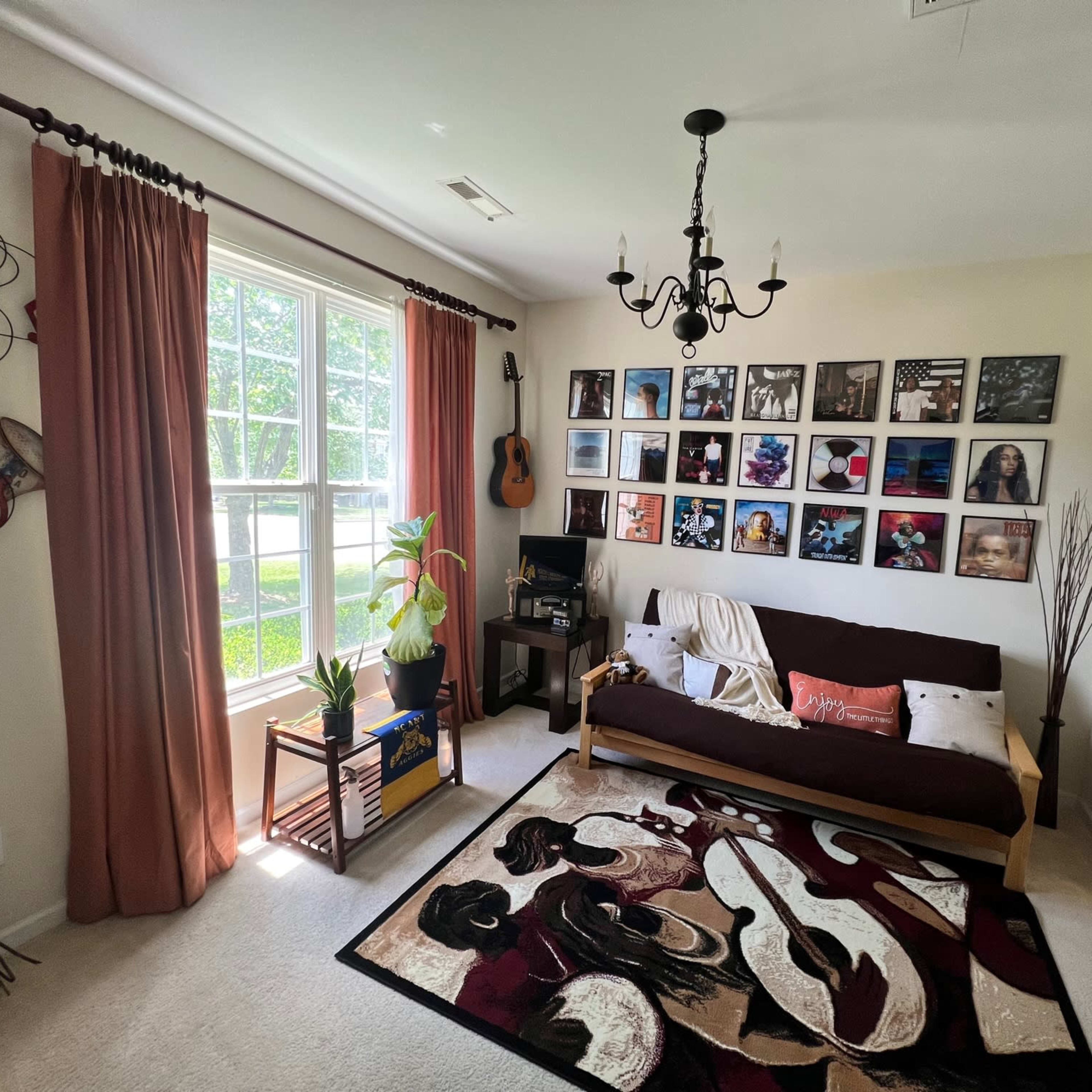 A cozy living room with a sofa bed, a colorful area rug, a wall of framed photographs, and large windows with curtains.