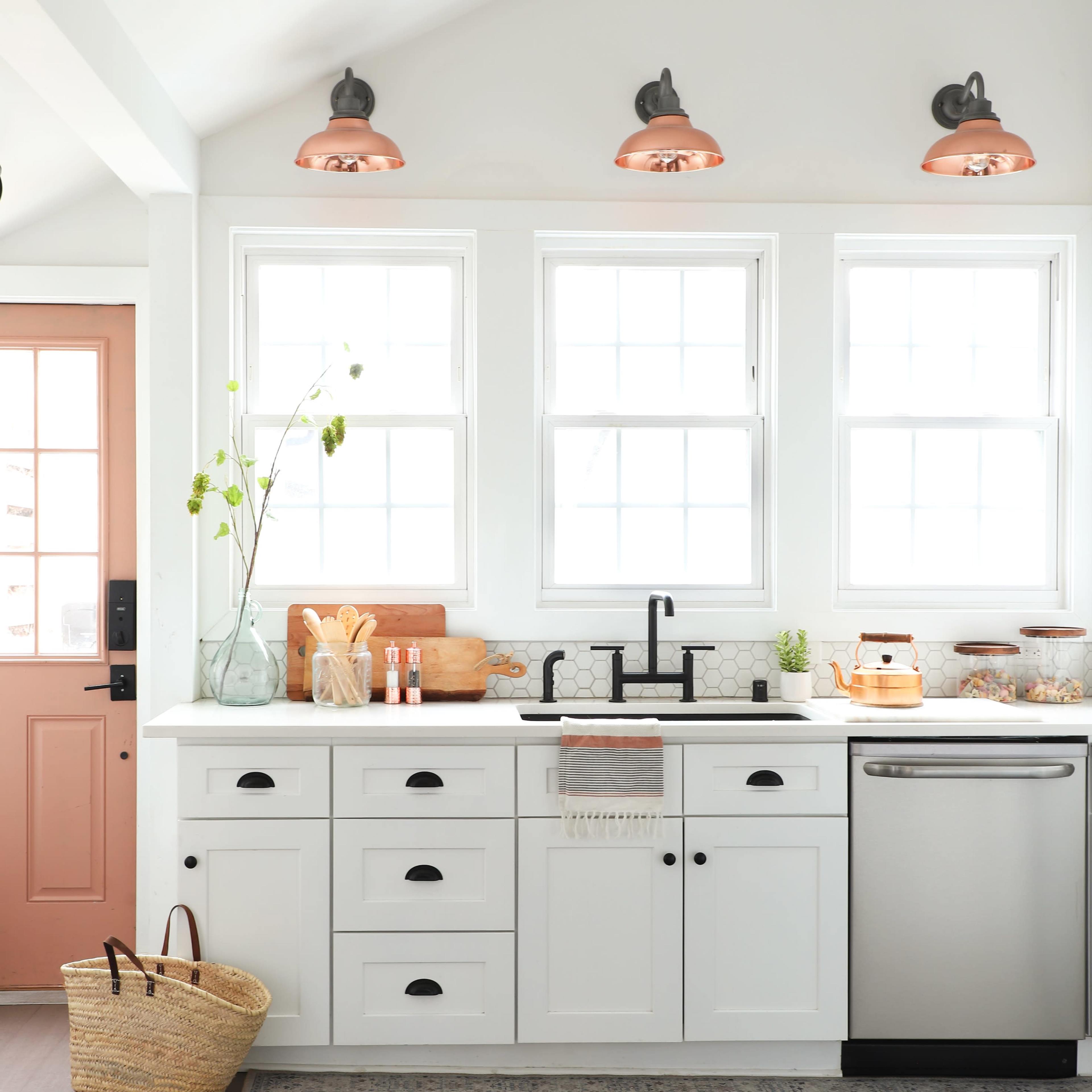 The kitchen features white cabinetry, a stainless steel dishwasher, a black faucet, and large windows with copper light fixtures above.