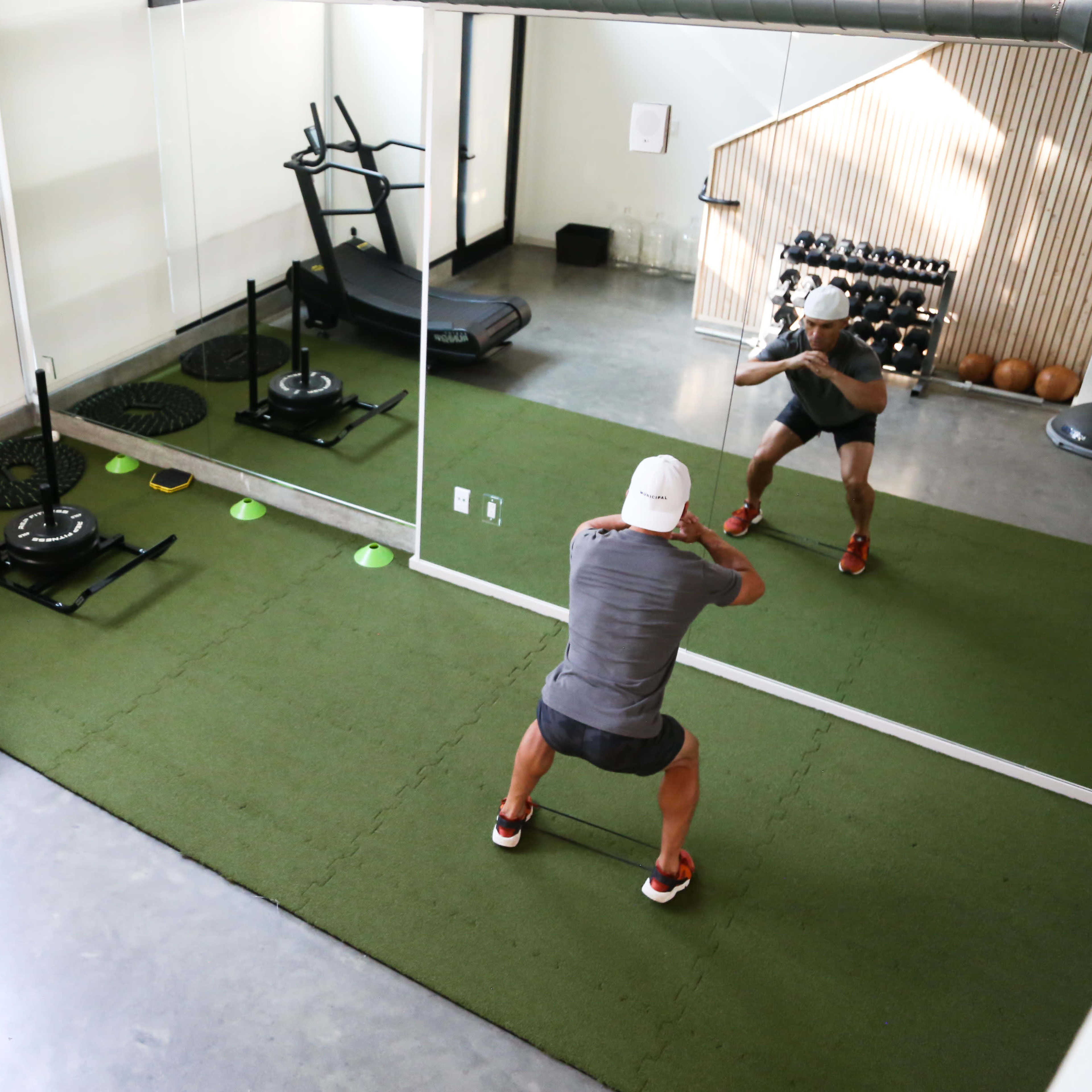 A person is performing an exercise in a modern gym with mirrored walls, a treadmill, and various fitness equipment.