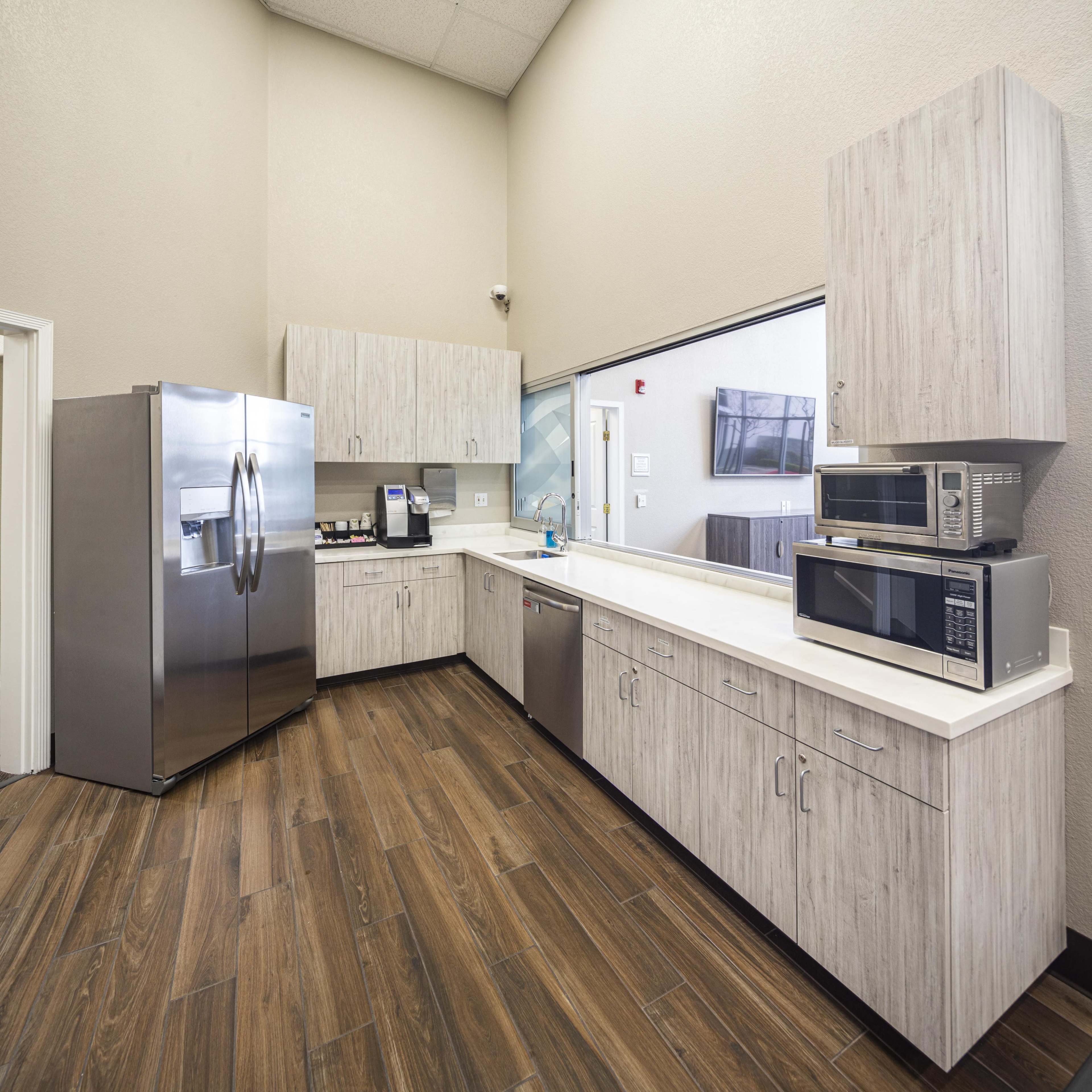 A modern kitchen featuring stainless steel appliances, including a refrigerator and microwave, with light wood cabinetry and a countertop.