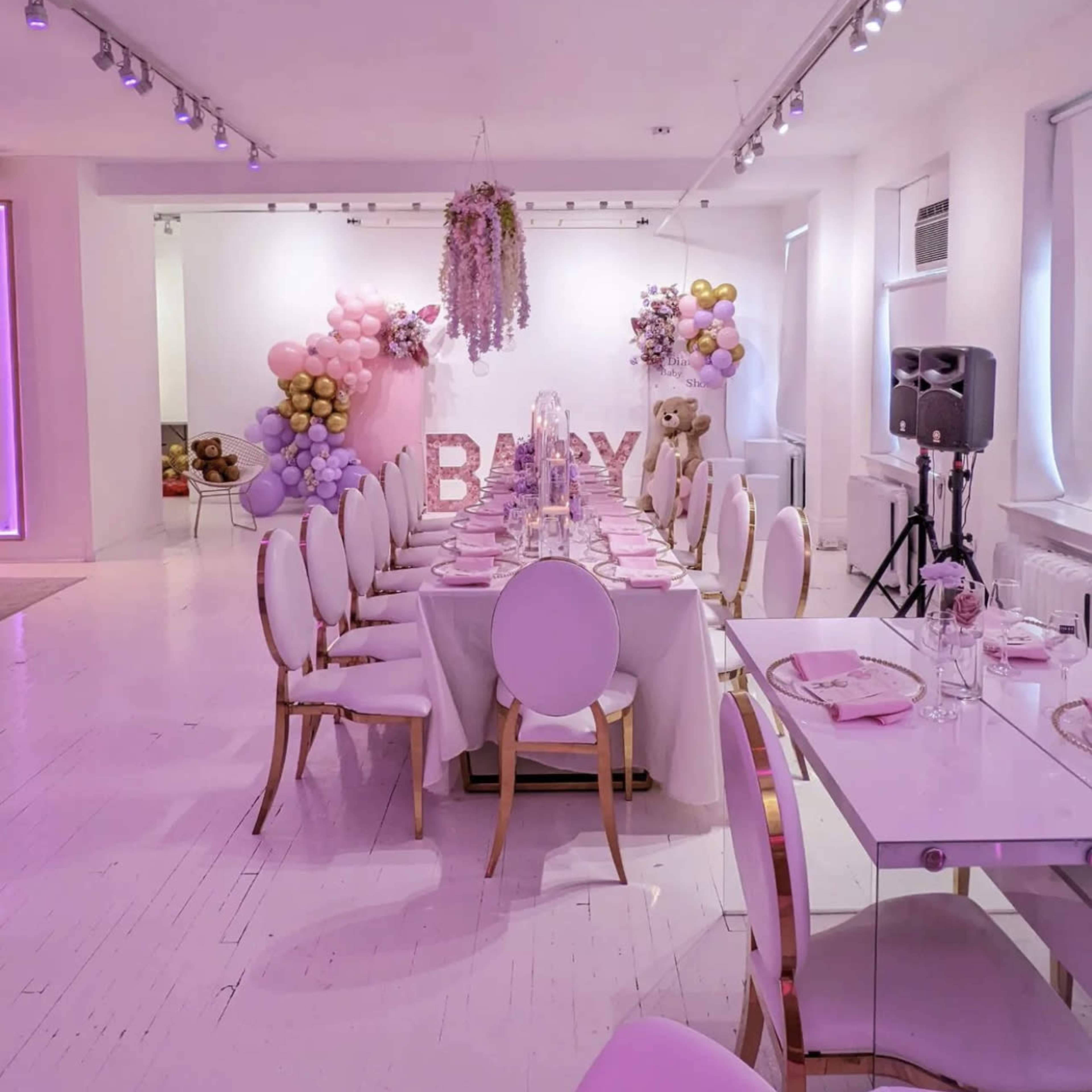 A elegantly arranged banquet table with pink decorations is set up in a venue adorned with balloons and a "BABY" sign in the background.