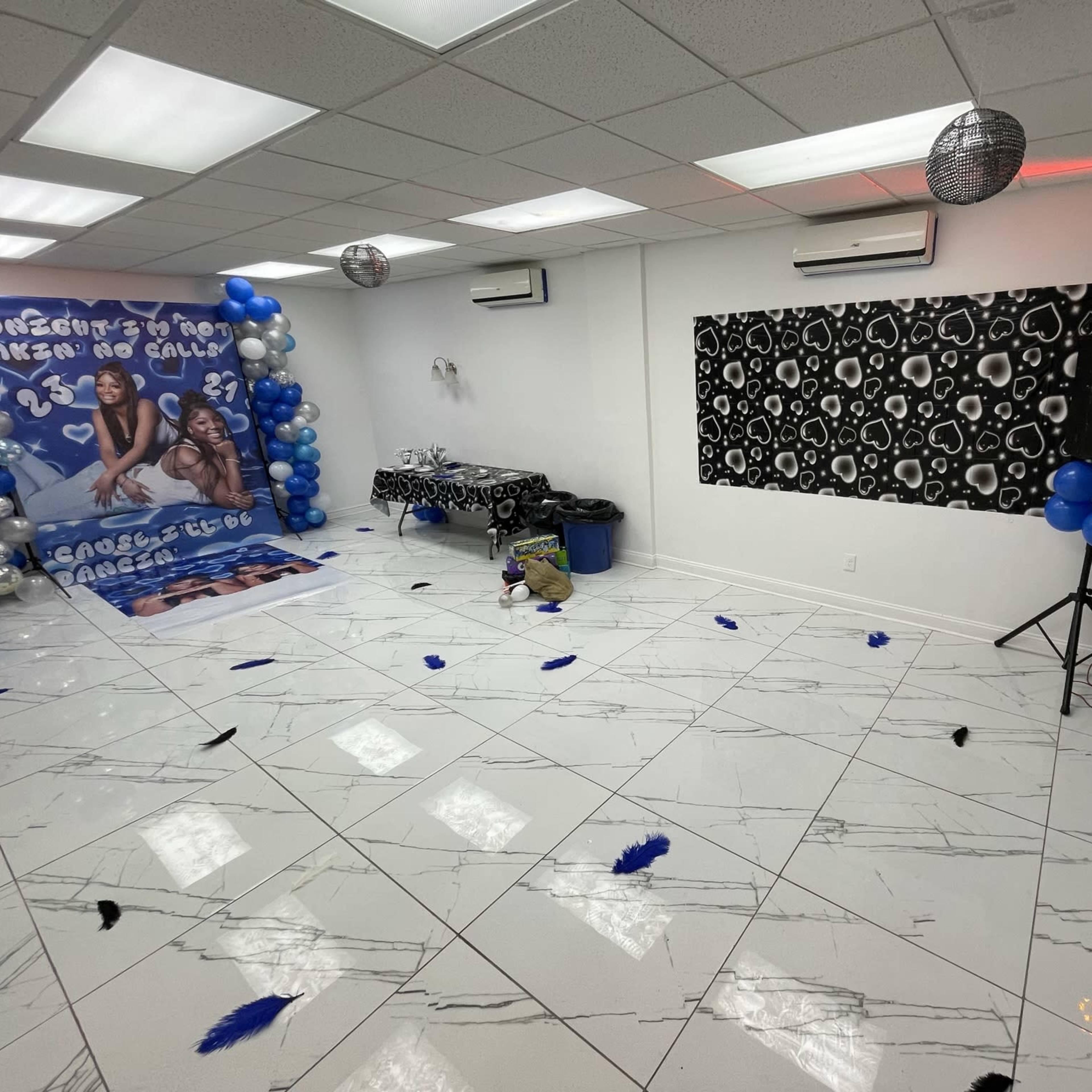 The room features a decorated space with blue and black balloons, a DJ setup, and a photo backdrop along one wall.