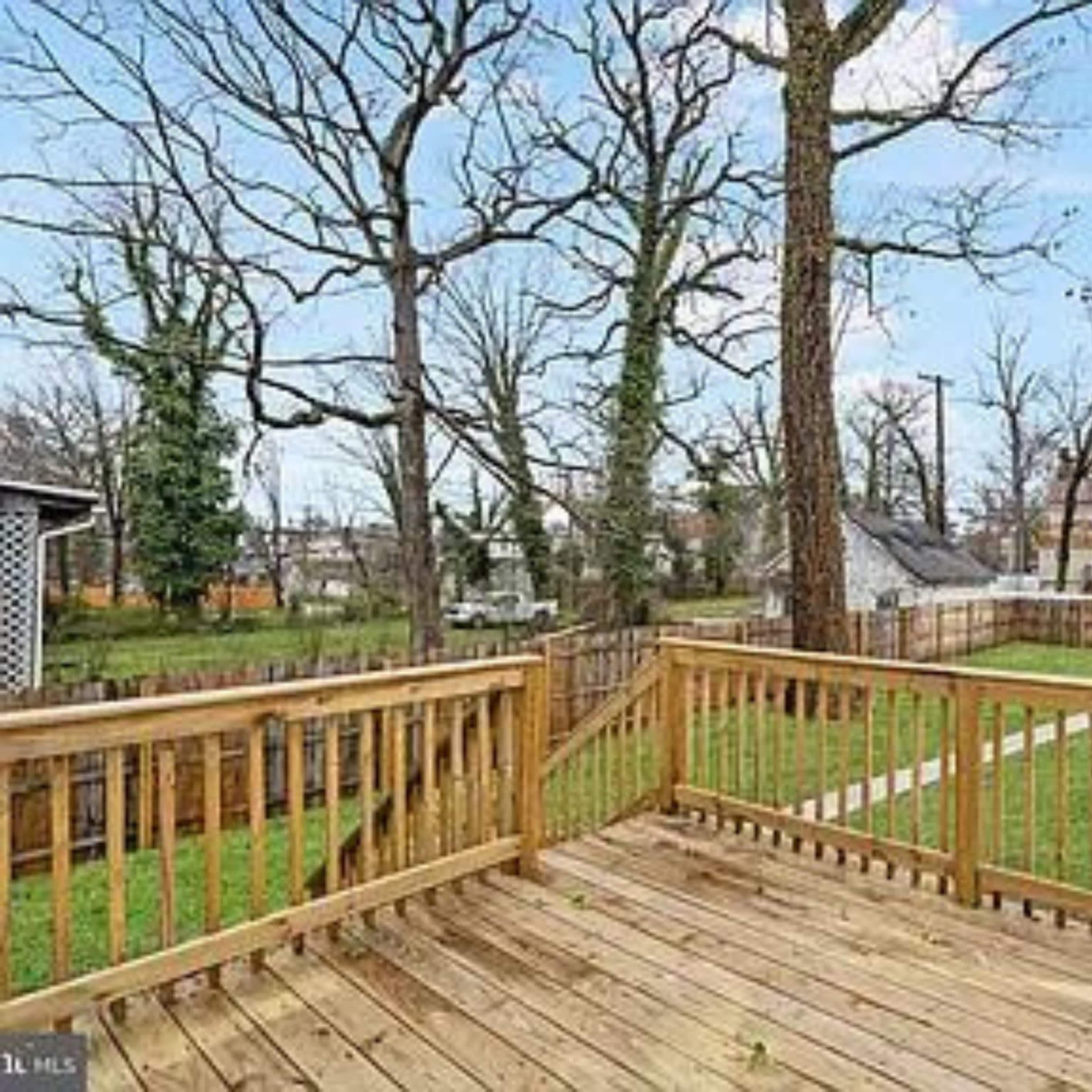 A wooden deck overlooking a grassy yard surrounded by wooden fencing and bare trees under a clear blue sky.