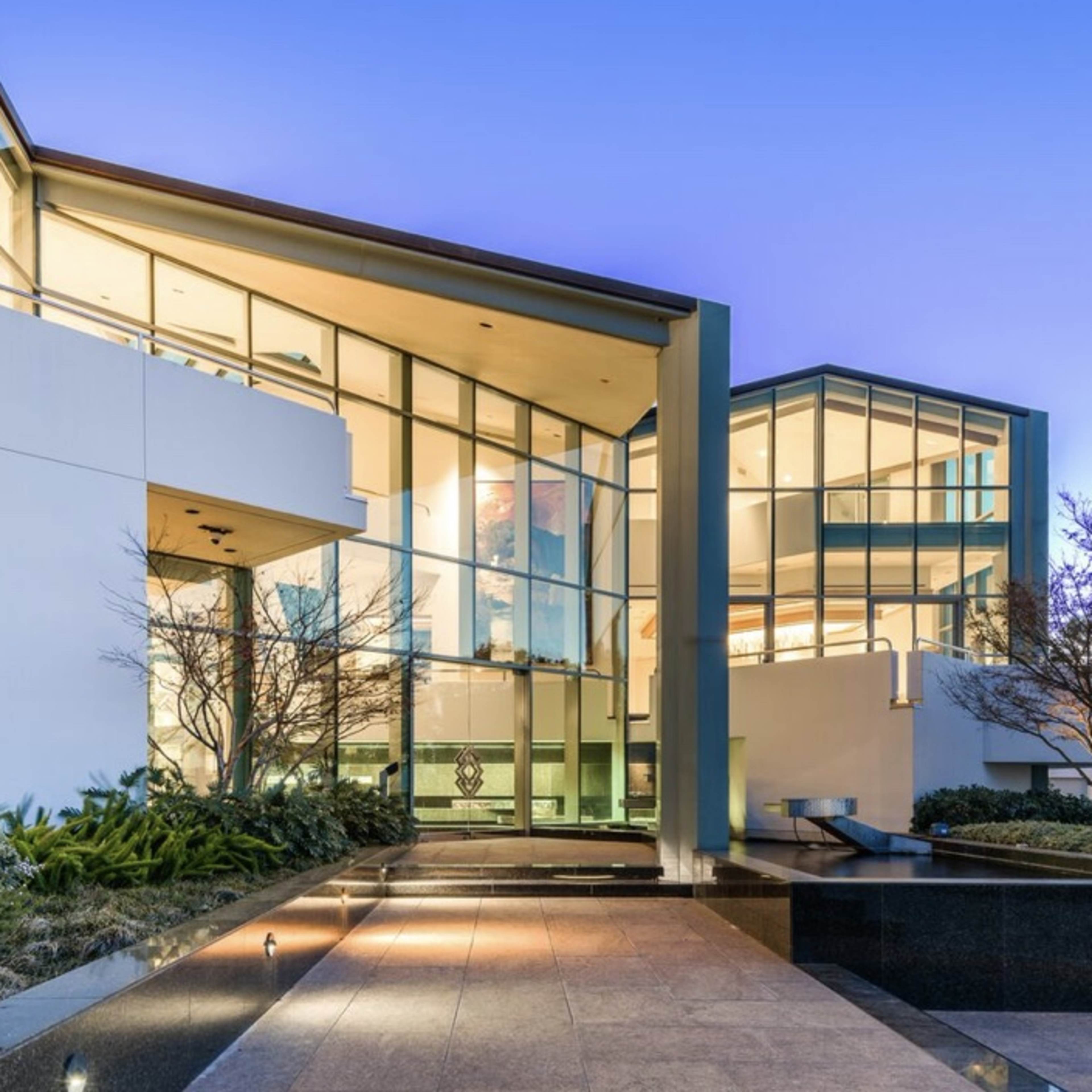 A modern glass-fronted building surrounded by landscaping at dusk.
