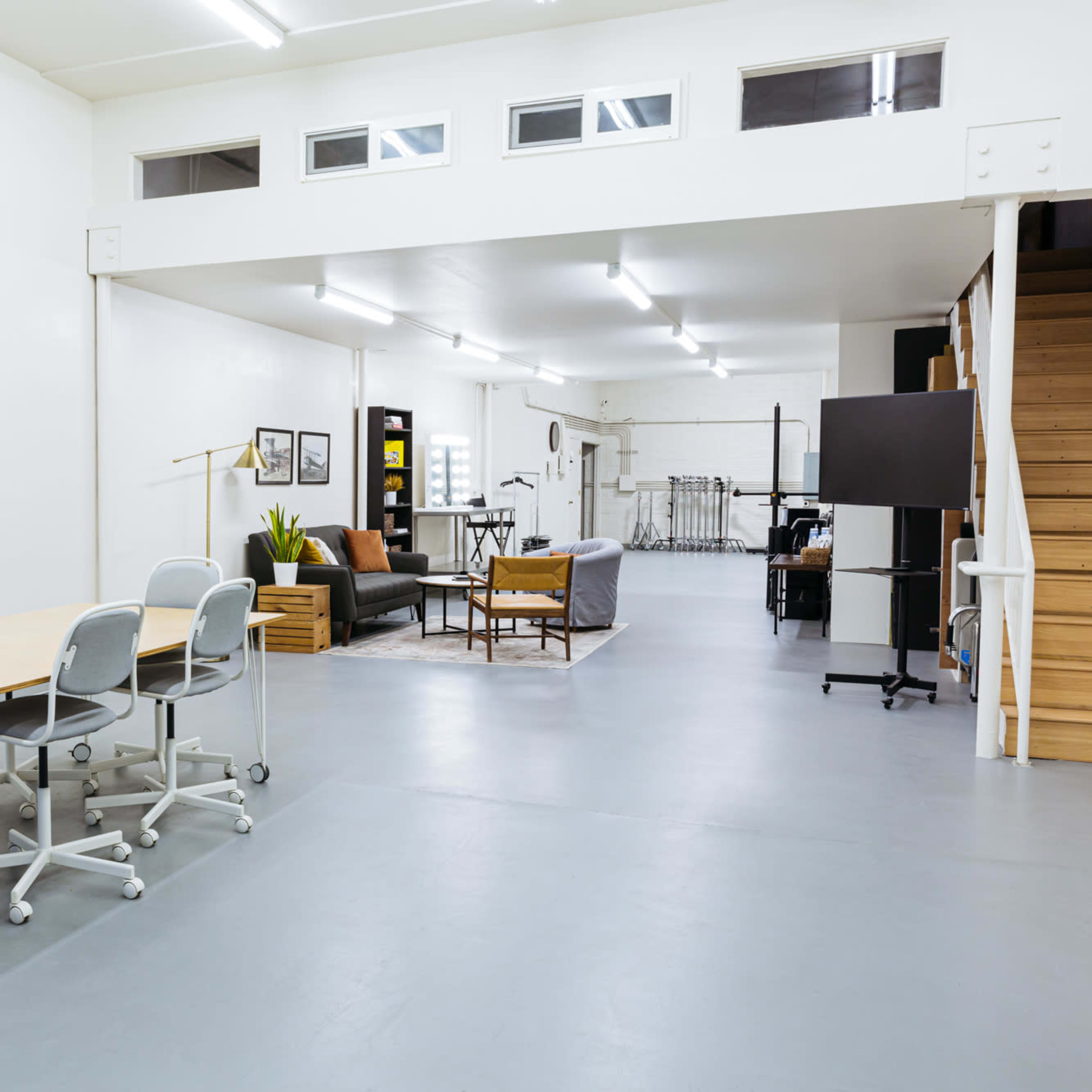 A spacious, well-lit interior featuring a meeting area with a table and chairs on one side and a living space with seating and a staircase on the other.