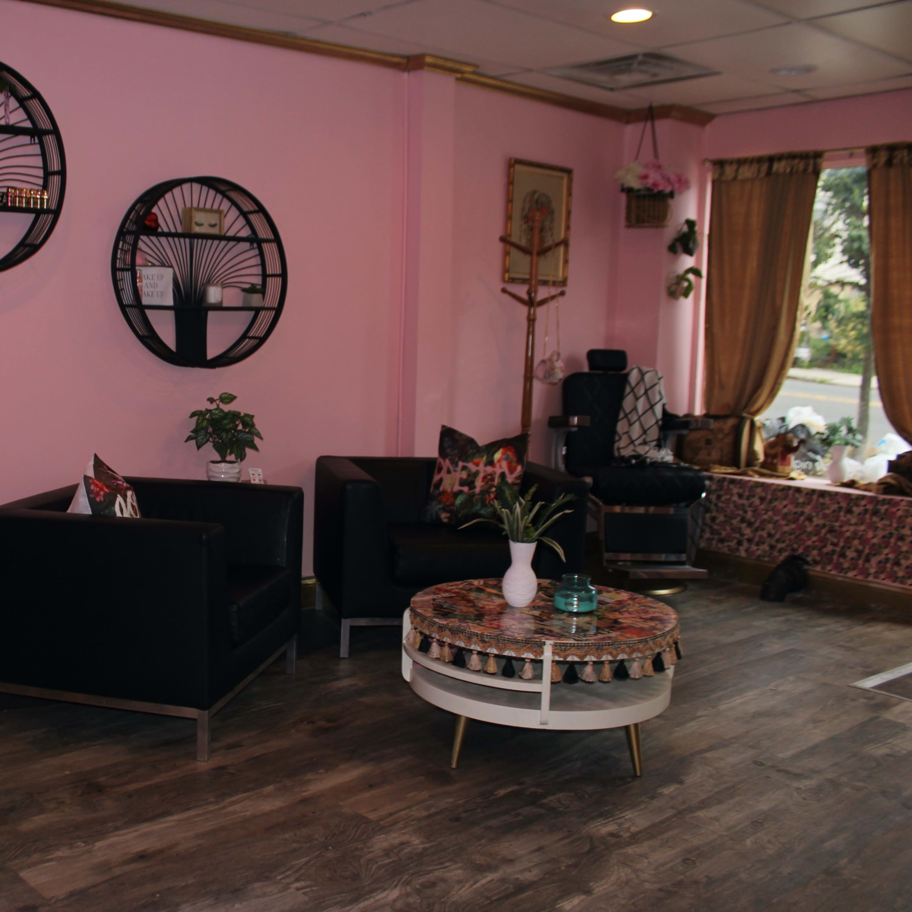 The interior of a pink-themed salon with black seating, decorative wall art, and a small table in the center.