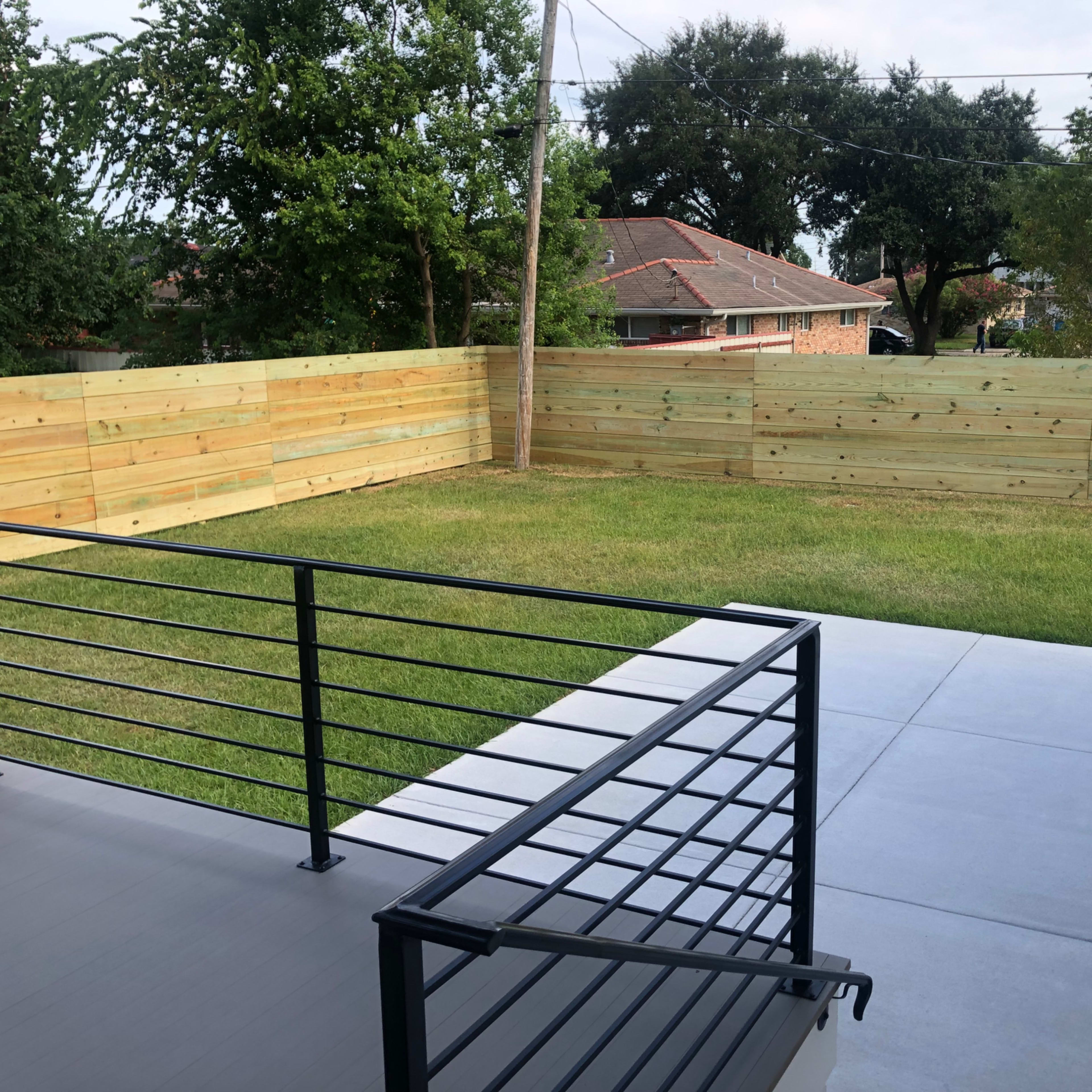 A patio area with a metal railing overlooking a fenced yard and grassy space.