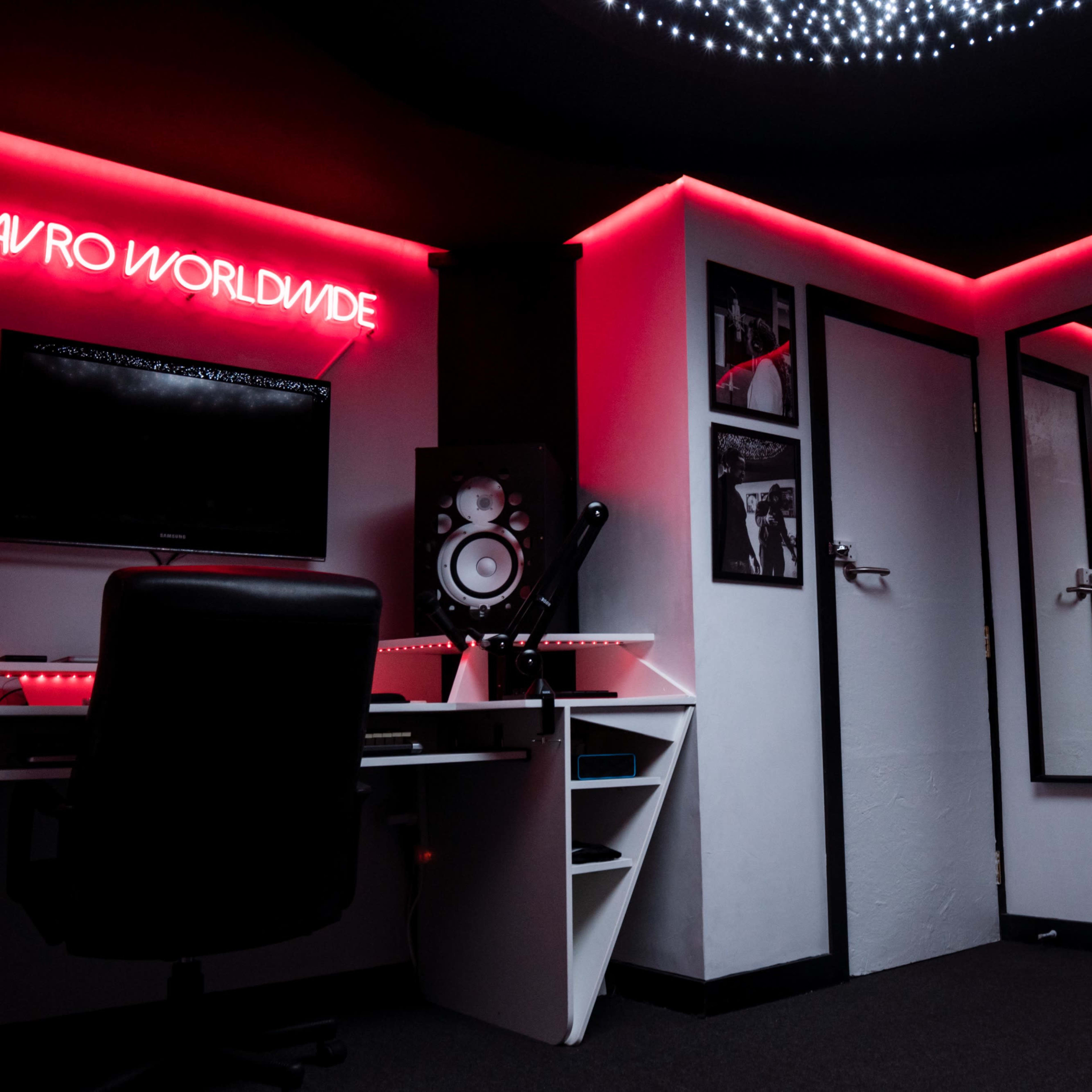 A dimly lit music studio with a computer setup, speakers, and illuminated walls.