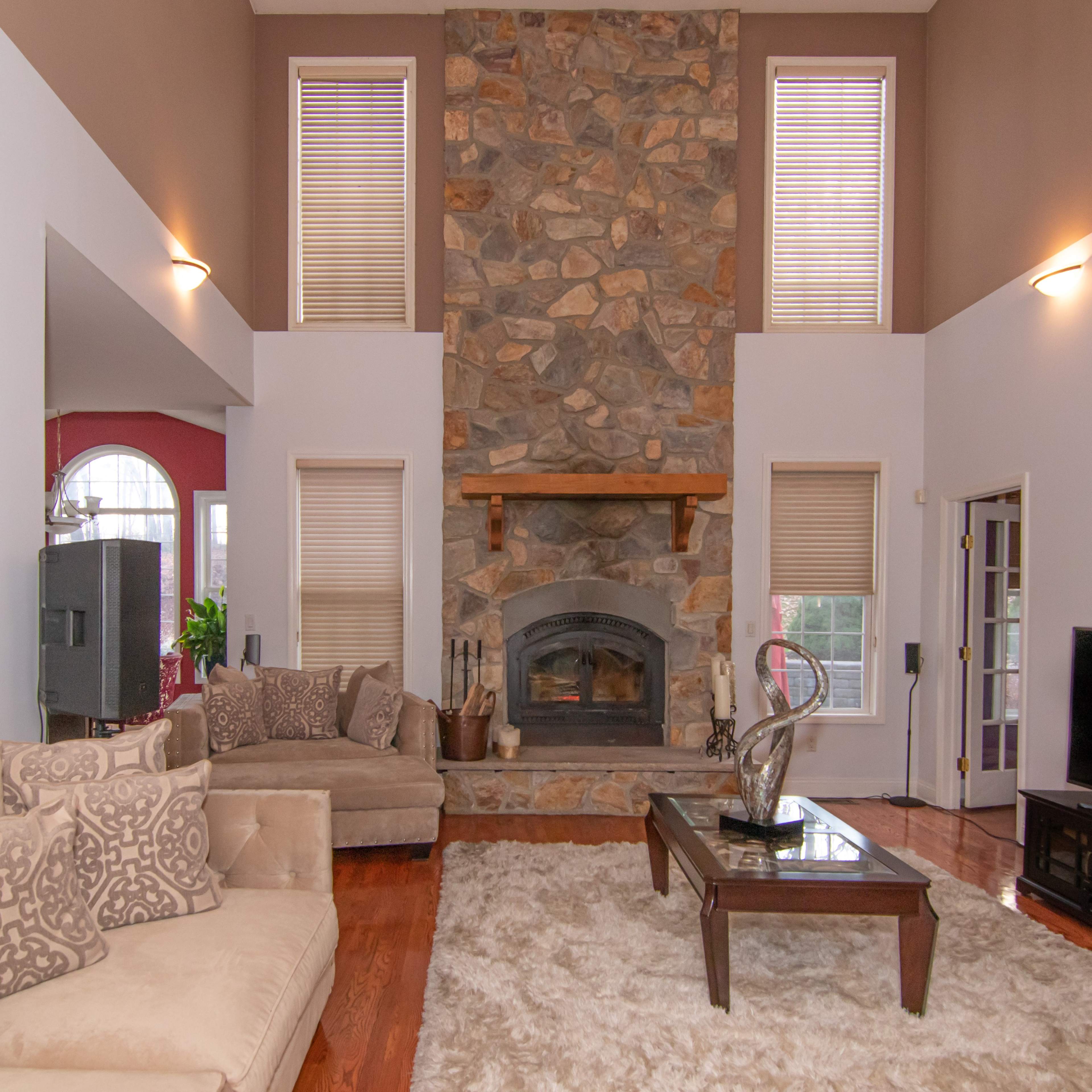 A spacious living room featuring a stone fireplace, large windows, and plush seating arranged around a coffee table.