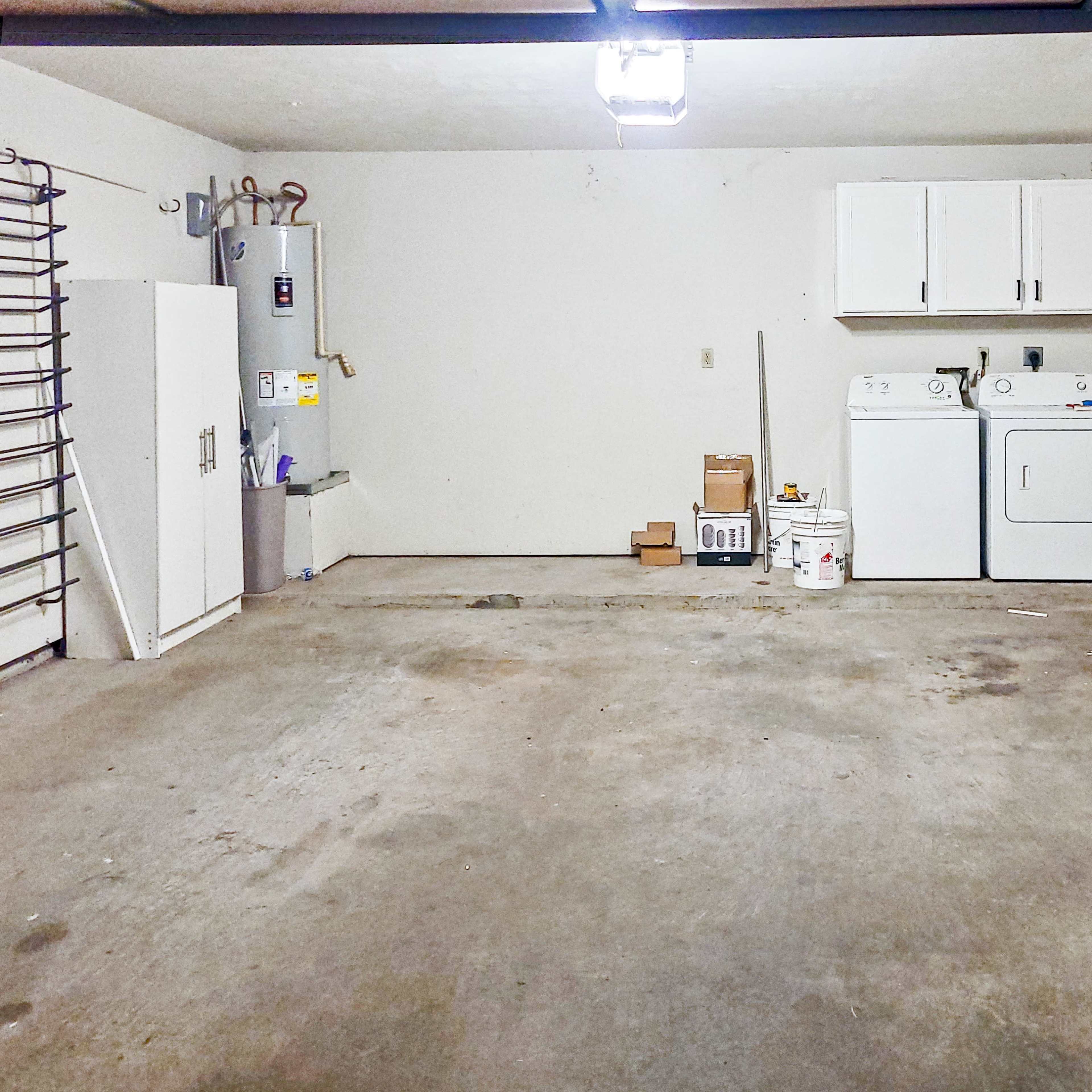 A spacious garage features a washer and dryer along one wall, with storage cabinets and a hot water heater nearby.