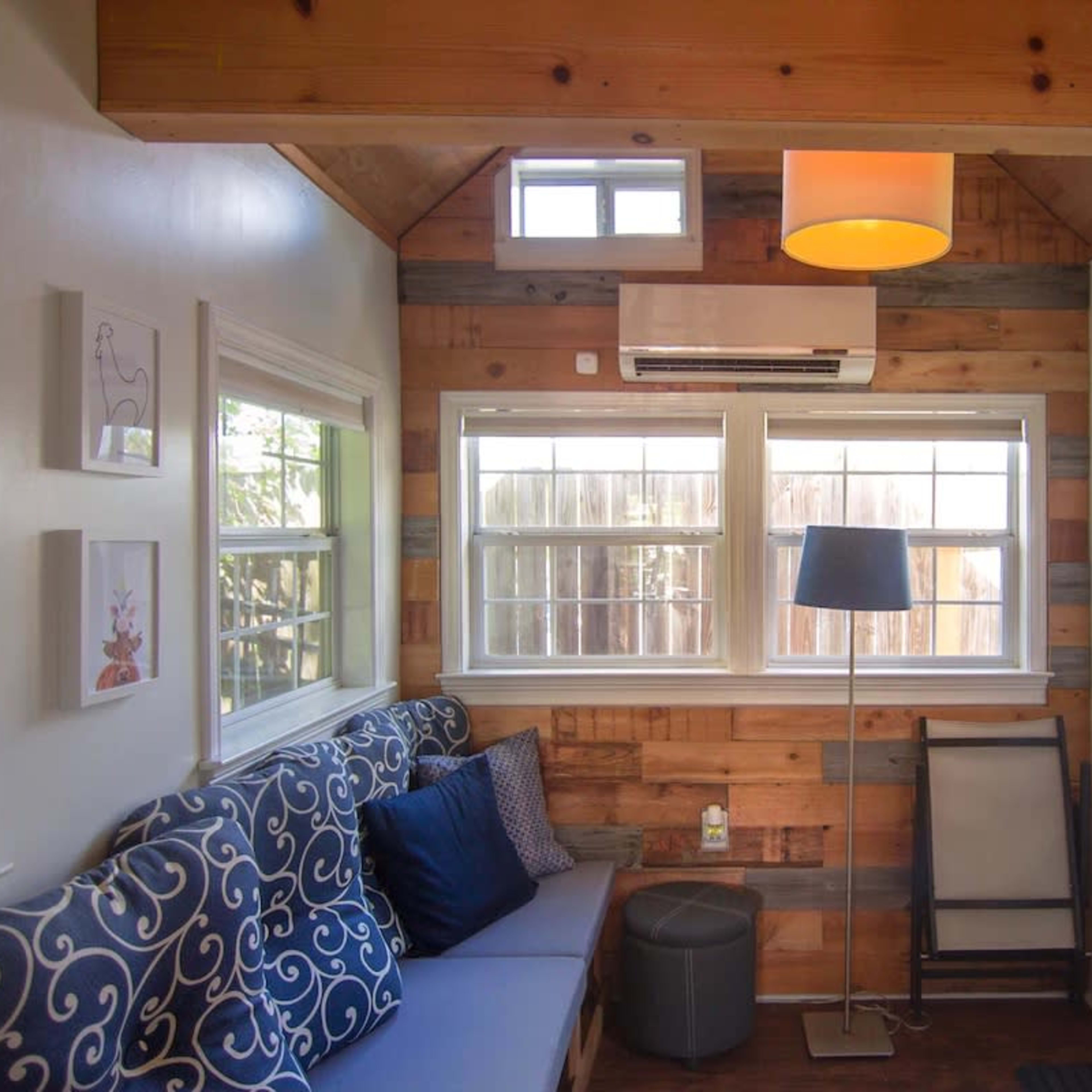 A cozy interior of a small room featuring a blue sofa with decorative pillows, a wooden accent wall, a lamp, a television, and a door leading outside.
